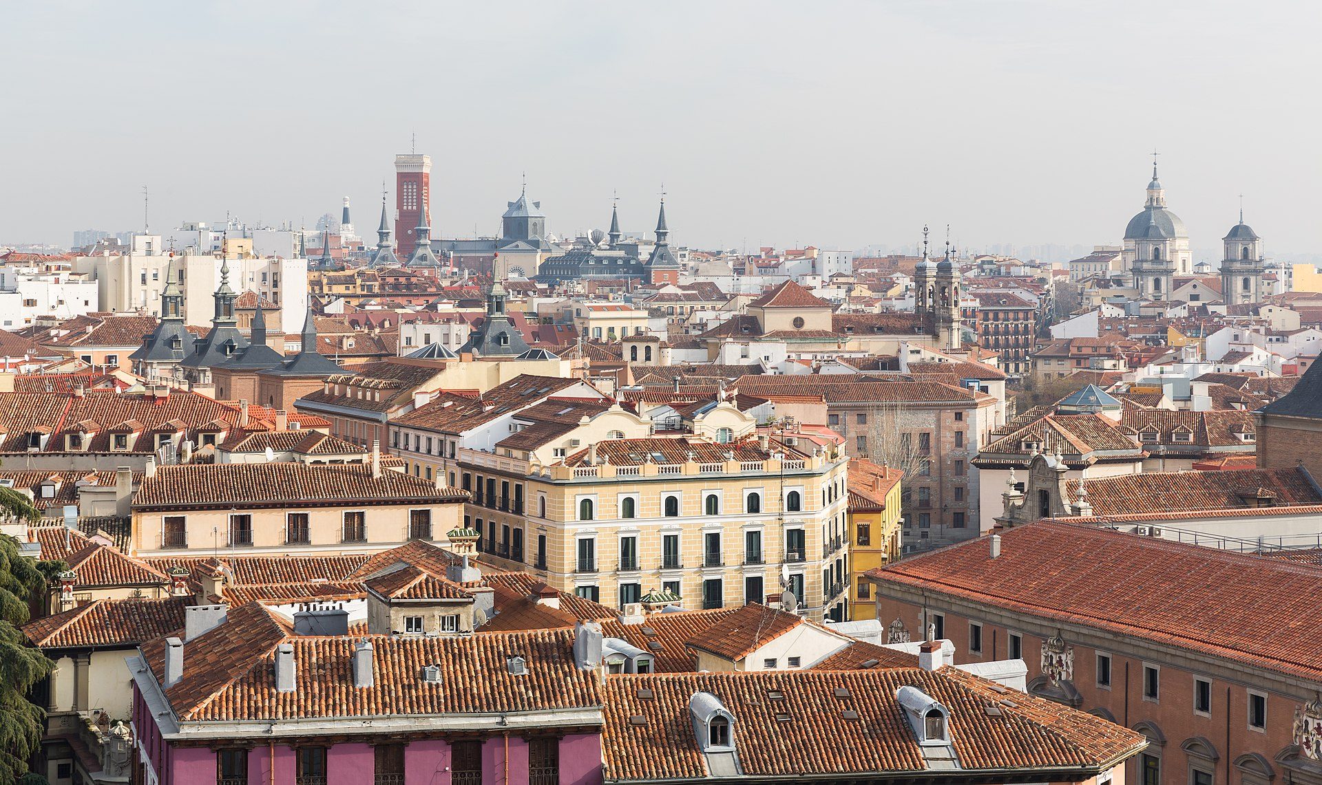 Panoramic city view from a spacious rooftop room with terracotta tiles and surrounding architecture.