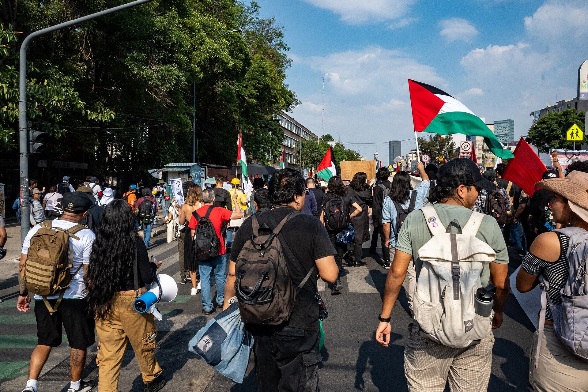Alt text: A group of people walking in a city street with flags and backpacks.