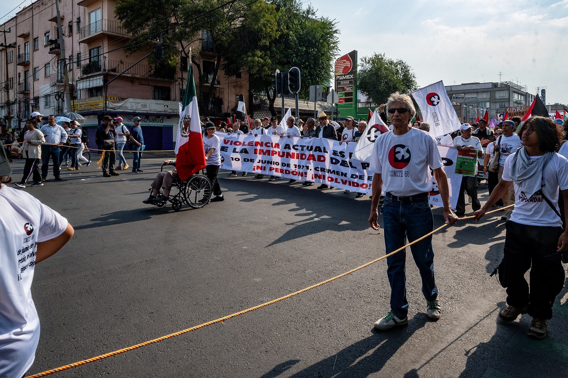 Alt text: Outdoor protest with participants holding banners and flags.