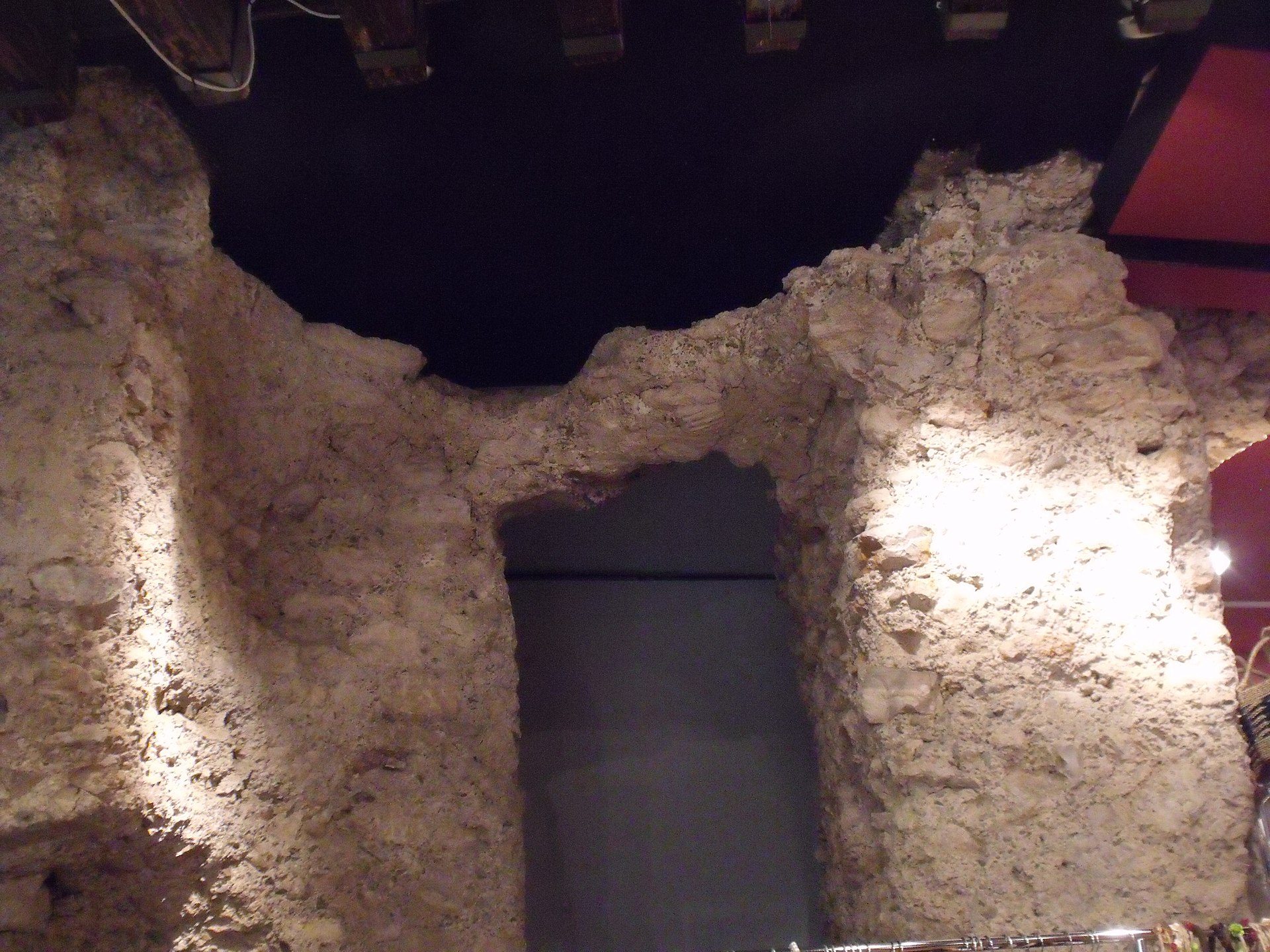Alt text: Interior view of rustic stone-walled room with arched doorway and modern lighting.