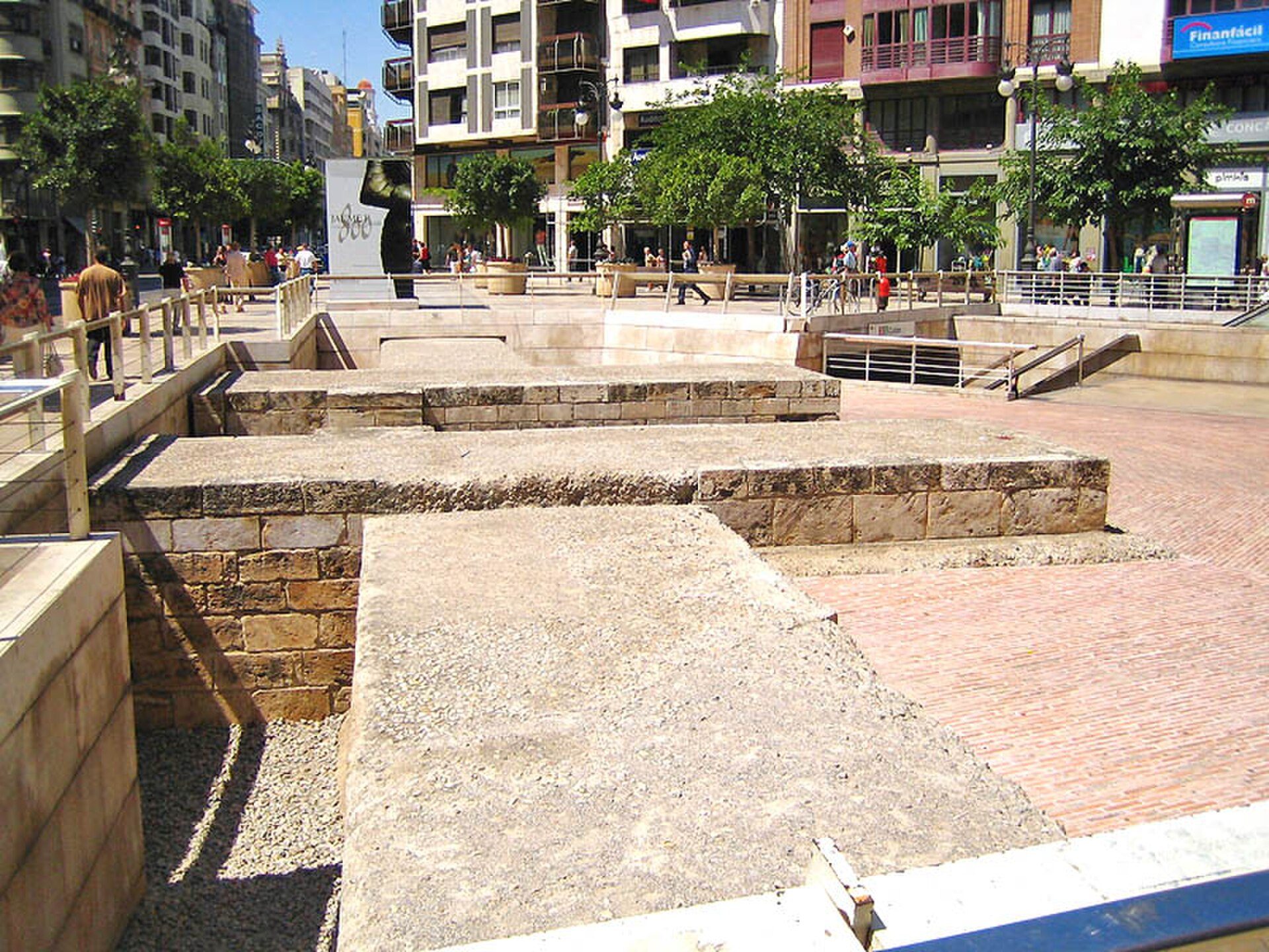 Alt text: Outdoor urban plaza with stone steps, trees, and modern buildings.