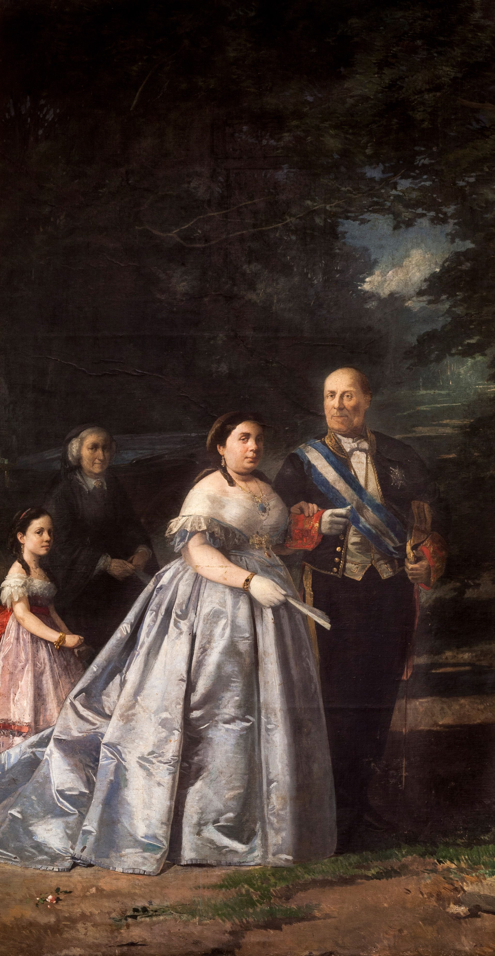 Alt text: A formal portrait of a family in historical attire, standing outdoors with trees in the background.