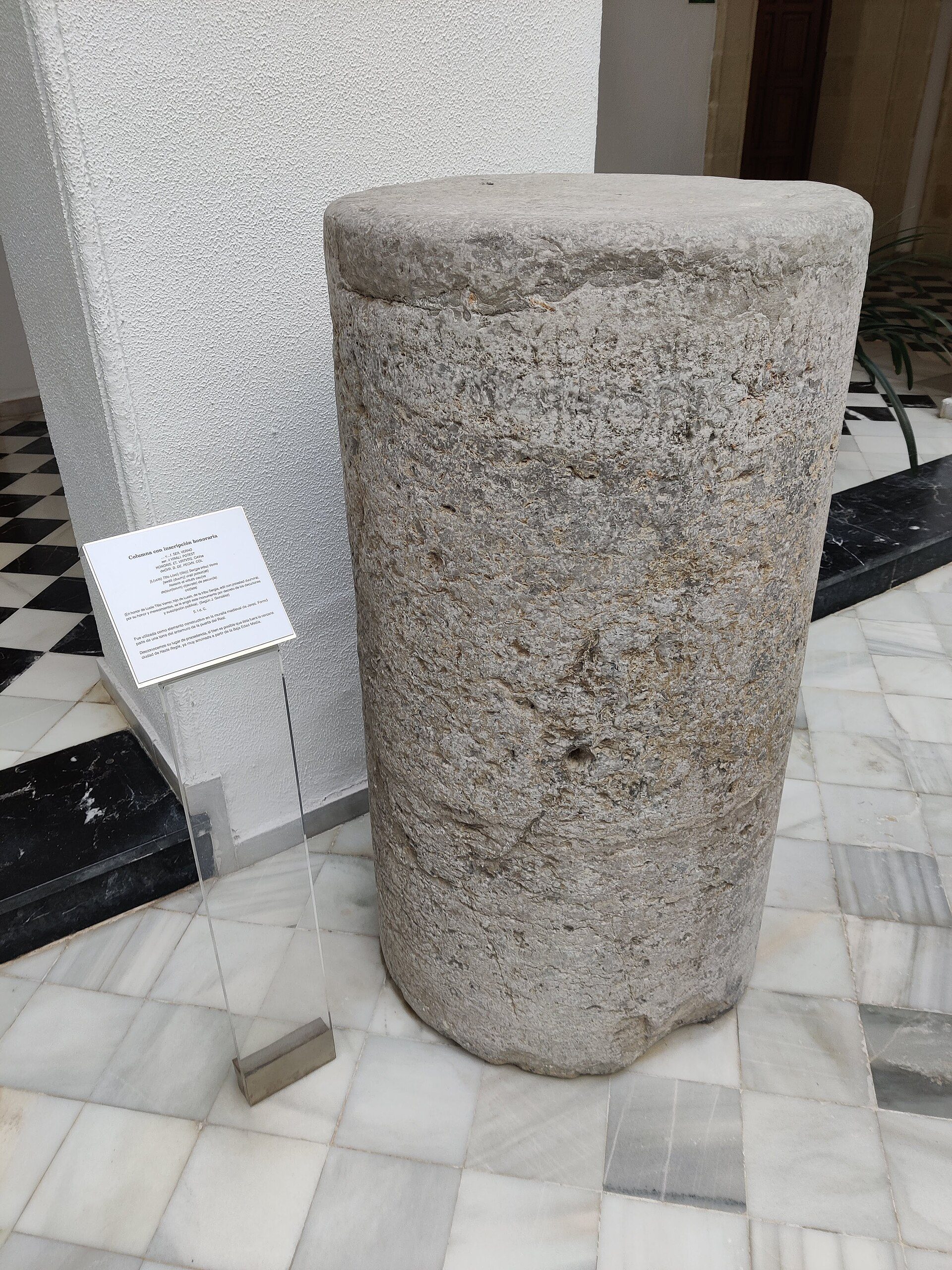 A stone pedestal with an informational plaque in a tiled room.