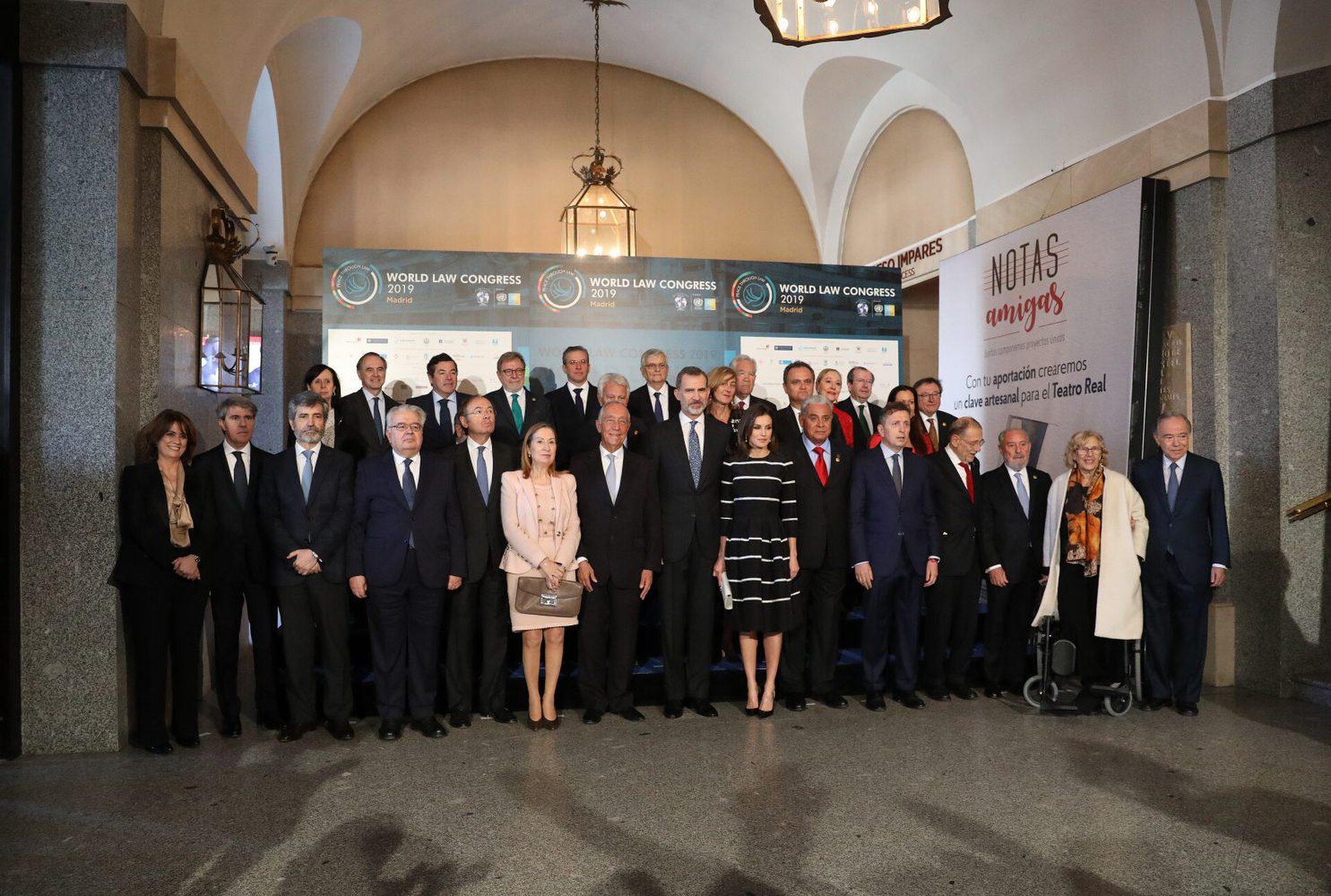 A group of people posing for a photo in a formal conference room with a chandelier and banners.