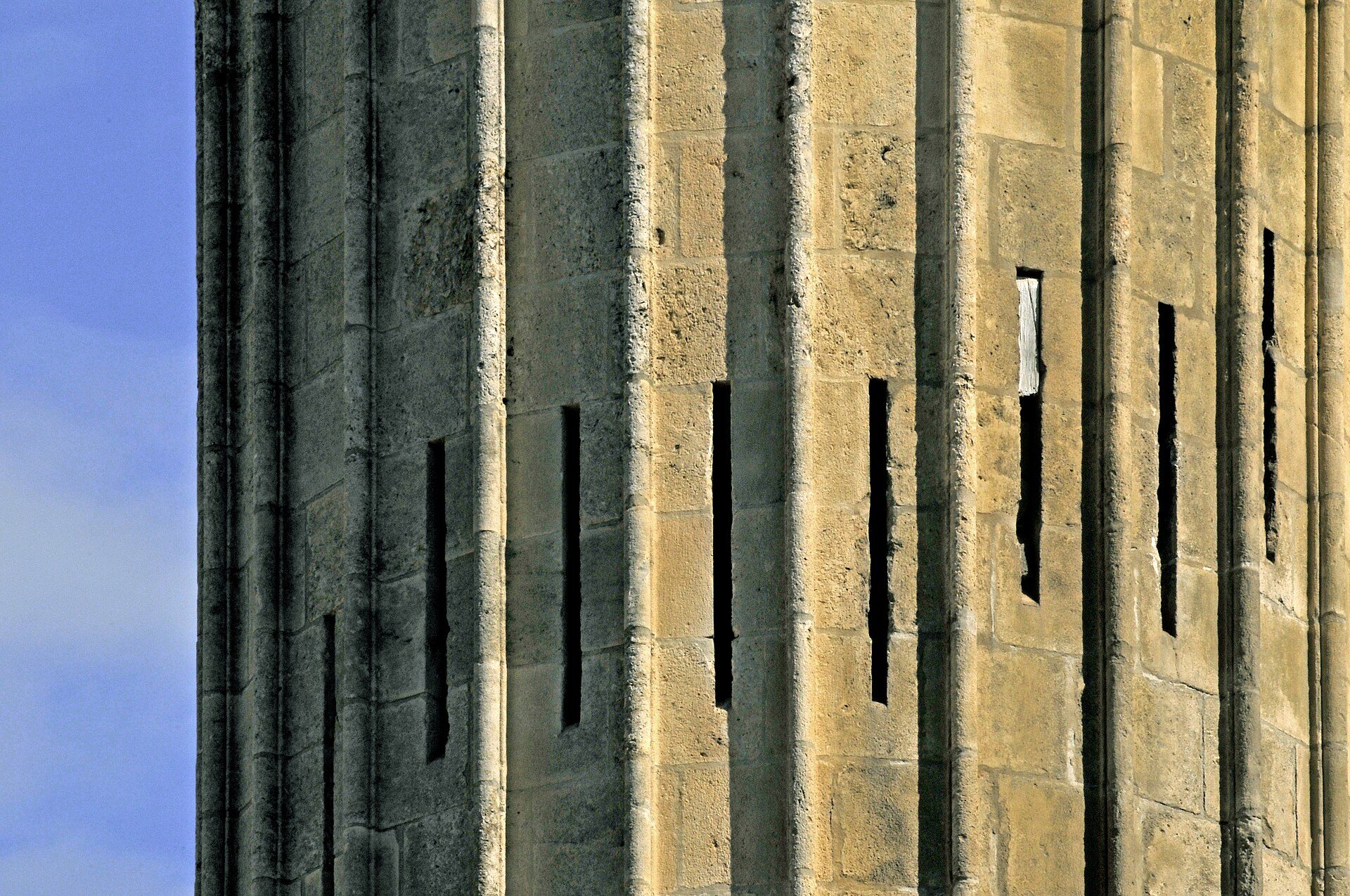 Alt text: Tall stone tower with narrow vertical windows and a clear blue sky view.