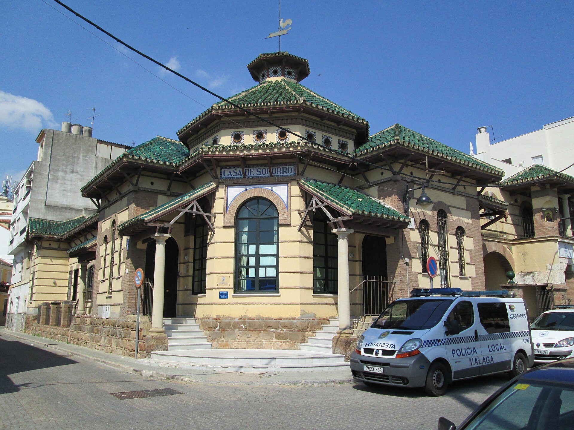 Traditional building with green roof, arched windows, and a police van parked outside.
