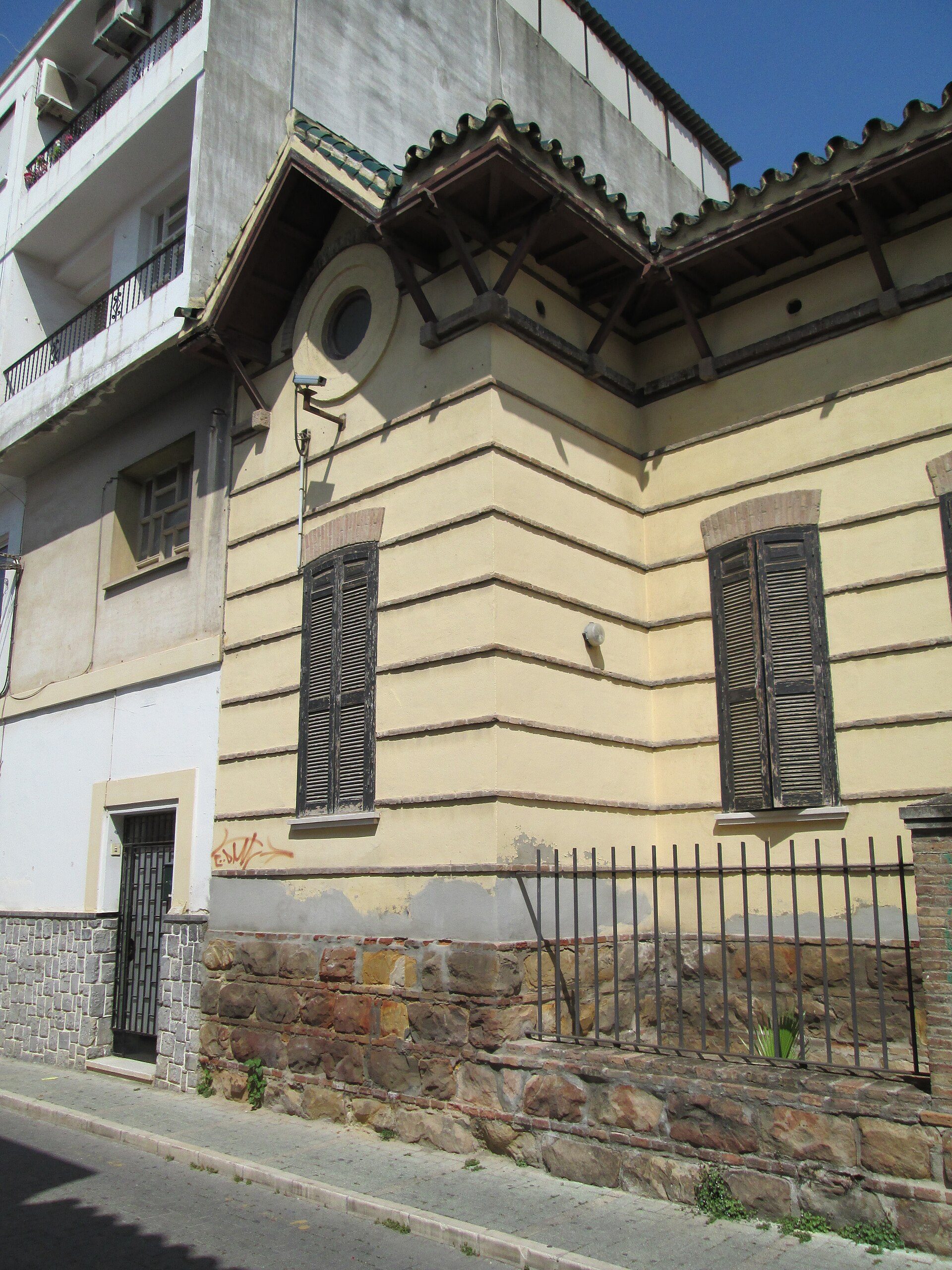 Two-story building with balconies, large windows, and a stone foundation.