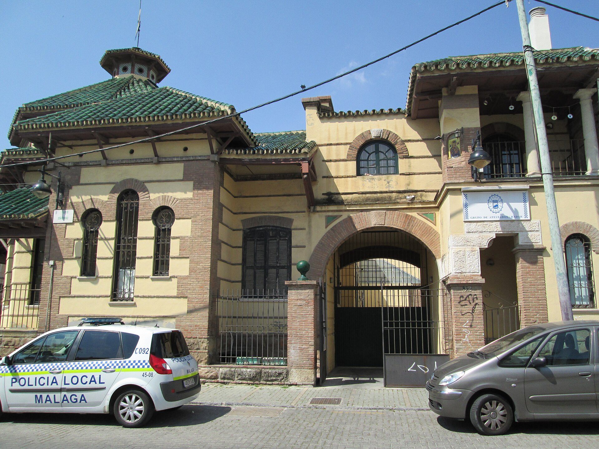 Traditional building with arched windows, green roof, and a police car parked in front.