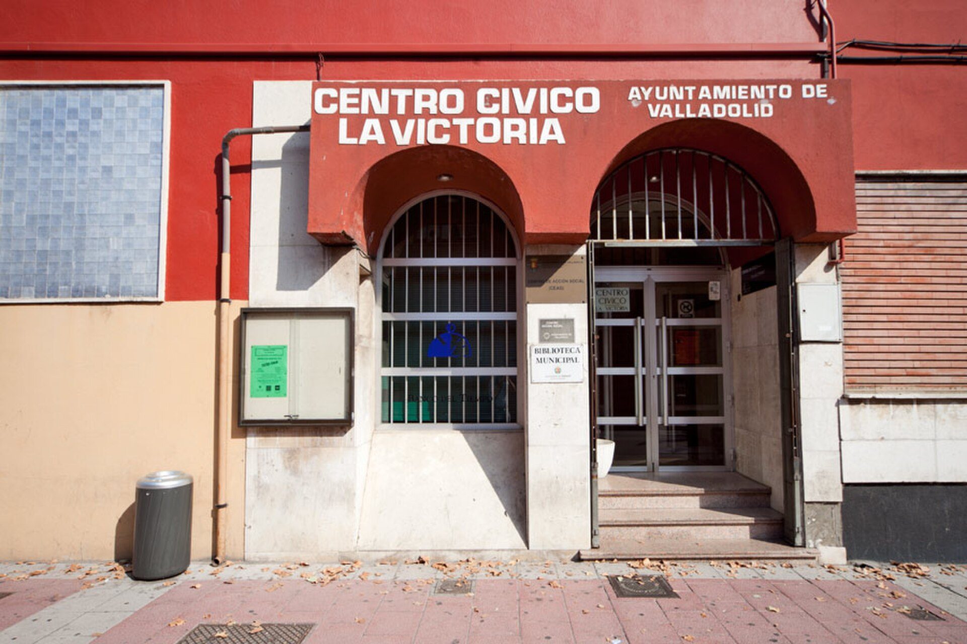 Alt text: Exterior of a red and beige building with a sign reading "CENTRO CIVICO LA VICTORIA" and barred windows.