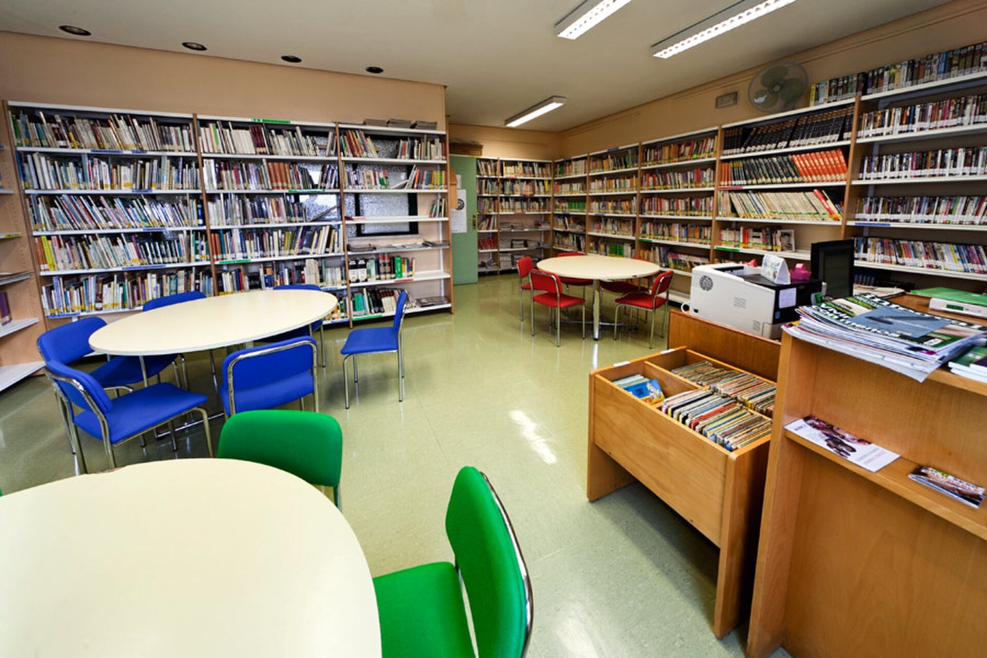 A well-lit library with bookshelves, tables, and chairs.