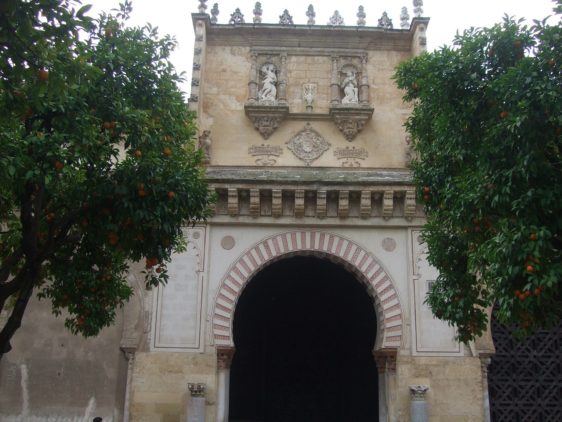Alt text: Historic archway with orange trees, featuring intricate carvings and a large central arch.