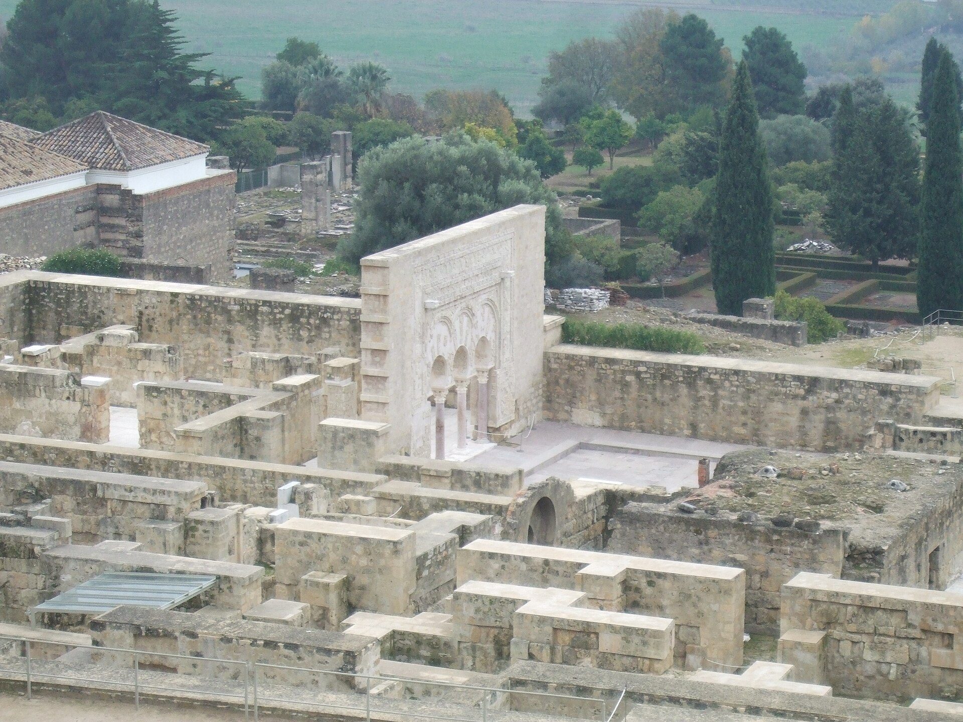 Ancient stone ruins with a courtyard, surrounded by greenery and distant fields.