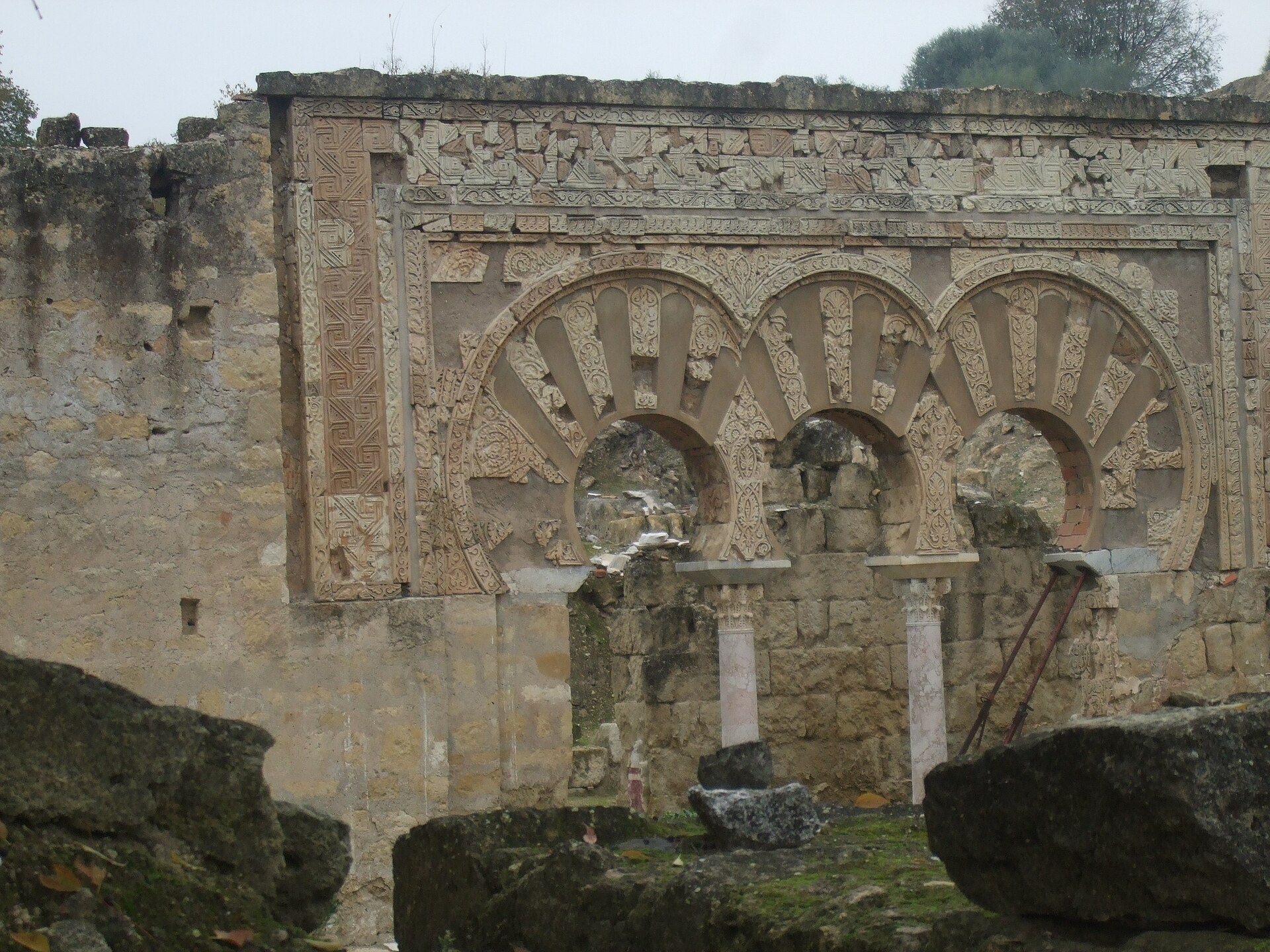 Historic stone archway with intricate carvings and overgrown vegetation.