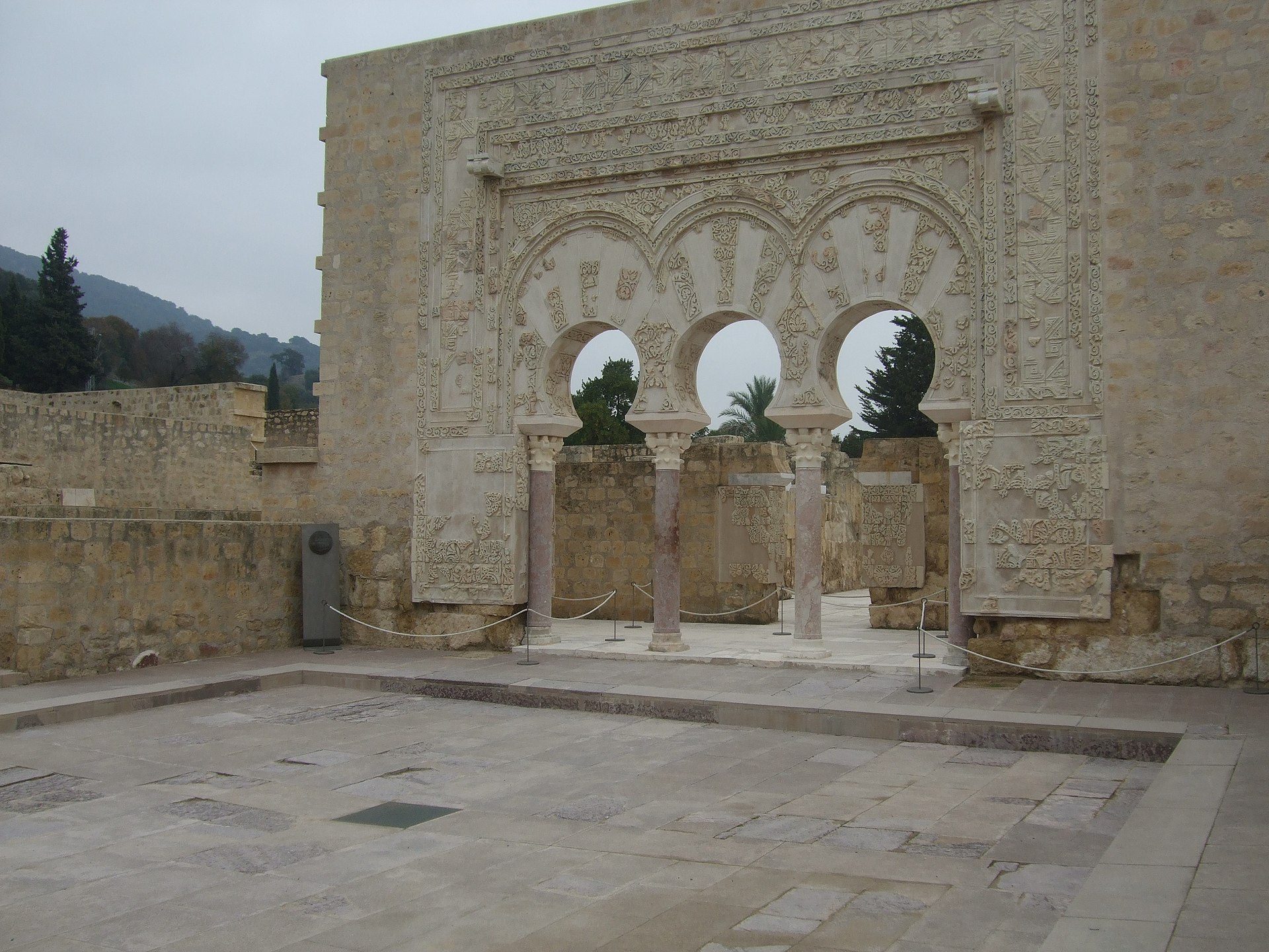 Historic courtyard with ornate stone arches, framed views of trees, and intricate carvings.