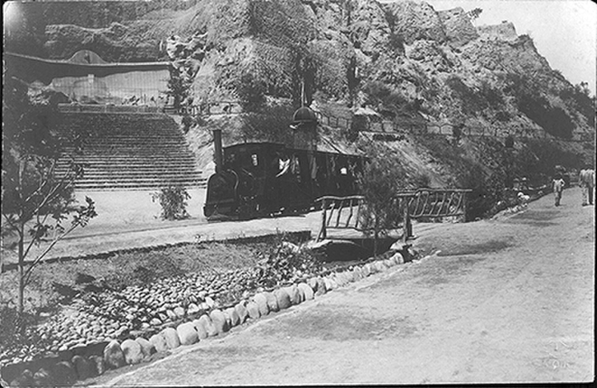 Old-fashioned train on tracks with a rocky hillside and steps in the background.