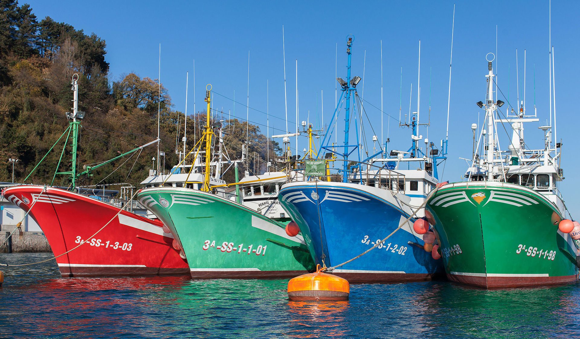 Colorful fishing boats docked in a serene harbor with clear blue skies.