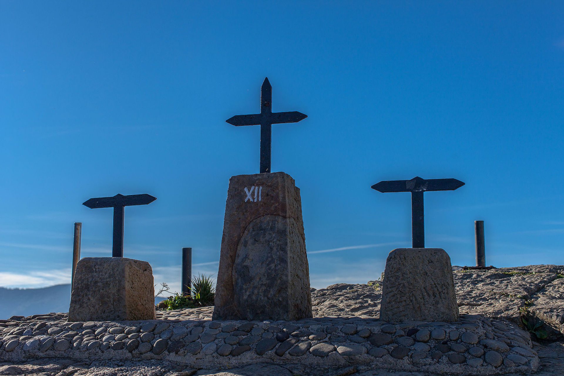 Alt text: Stone cross monument with clear blue sky and mountain view.