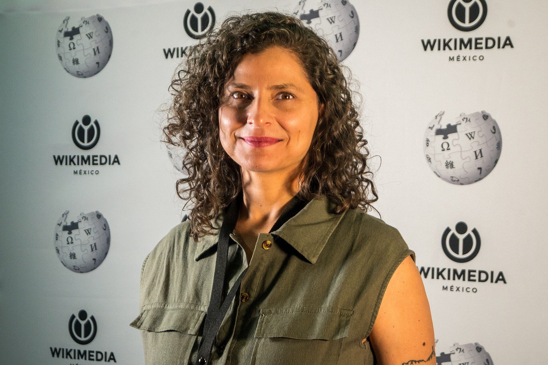 A woman with curly hair stands in front of a backdrop with the "Wikimedia Mexico" logo.