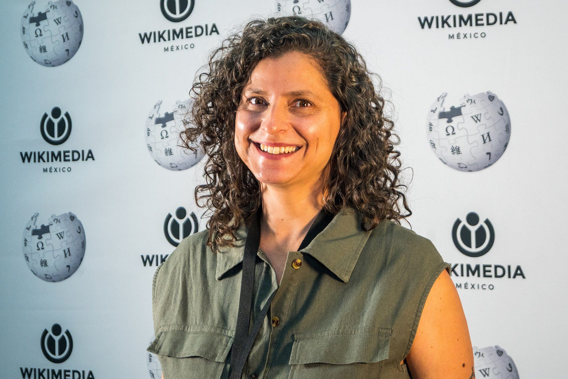 A woman with curly hair smiling in front of a WIKIMEDIA MEXICO backdrop.