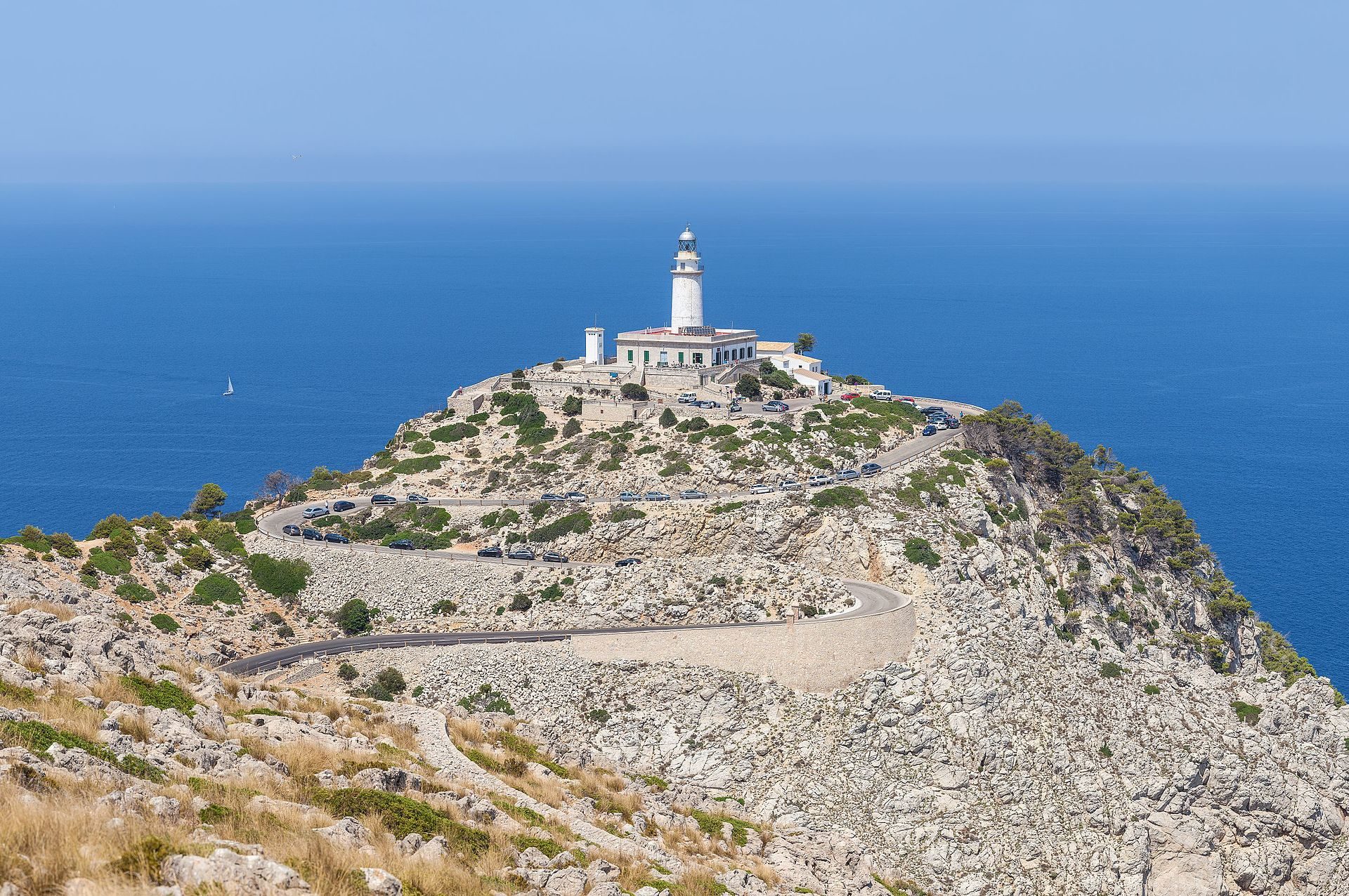 Lighthouse on rocky coast with ocean view, winding road, and clear blue sky.
