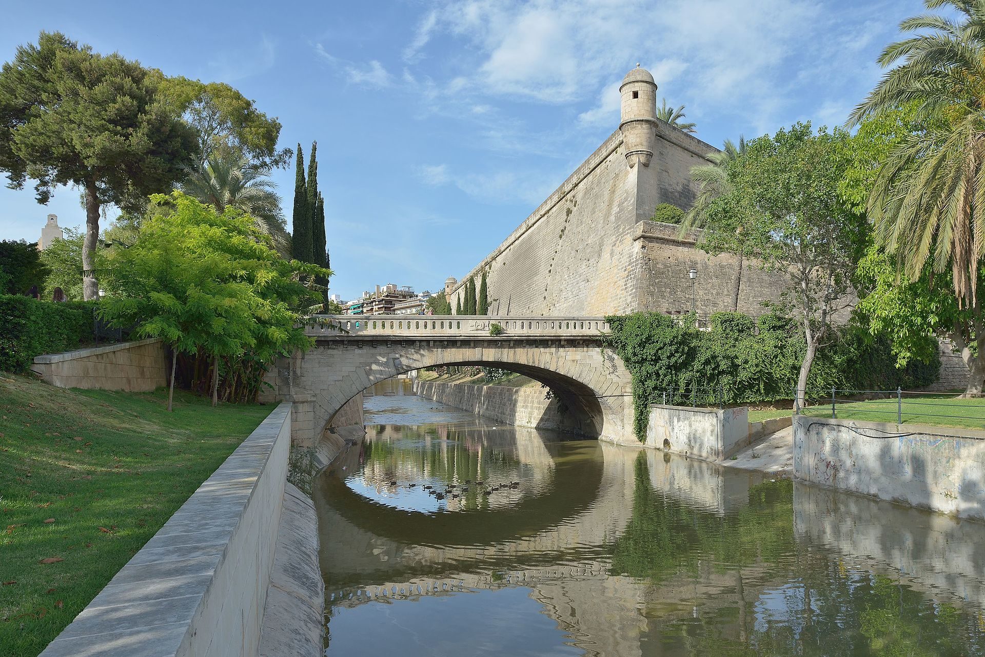 Alt text: Stone bridge with arches, river, greenery, and a tower in the background.