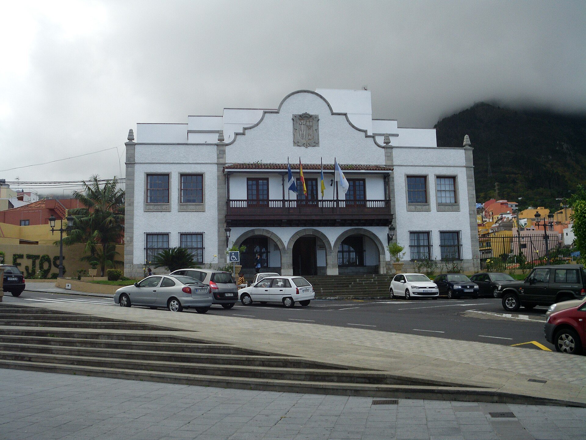 Traditional white building with balcony, flags, and mountain backdrop.