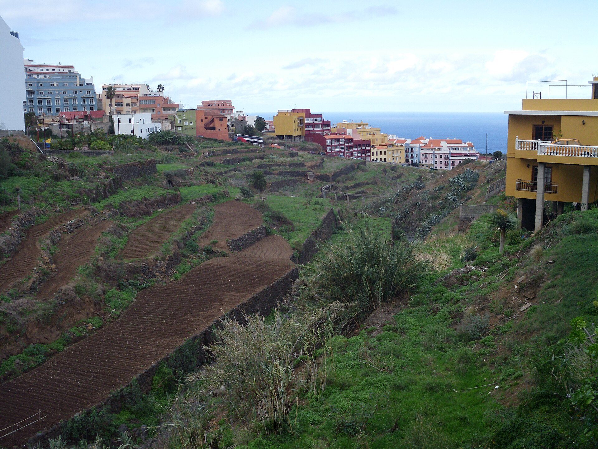 Alt text: Terraced garden view with colorful buildings and sea in the distance.