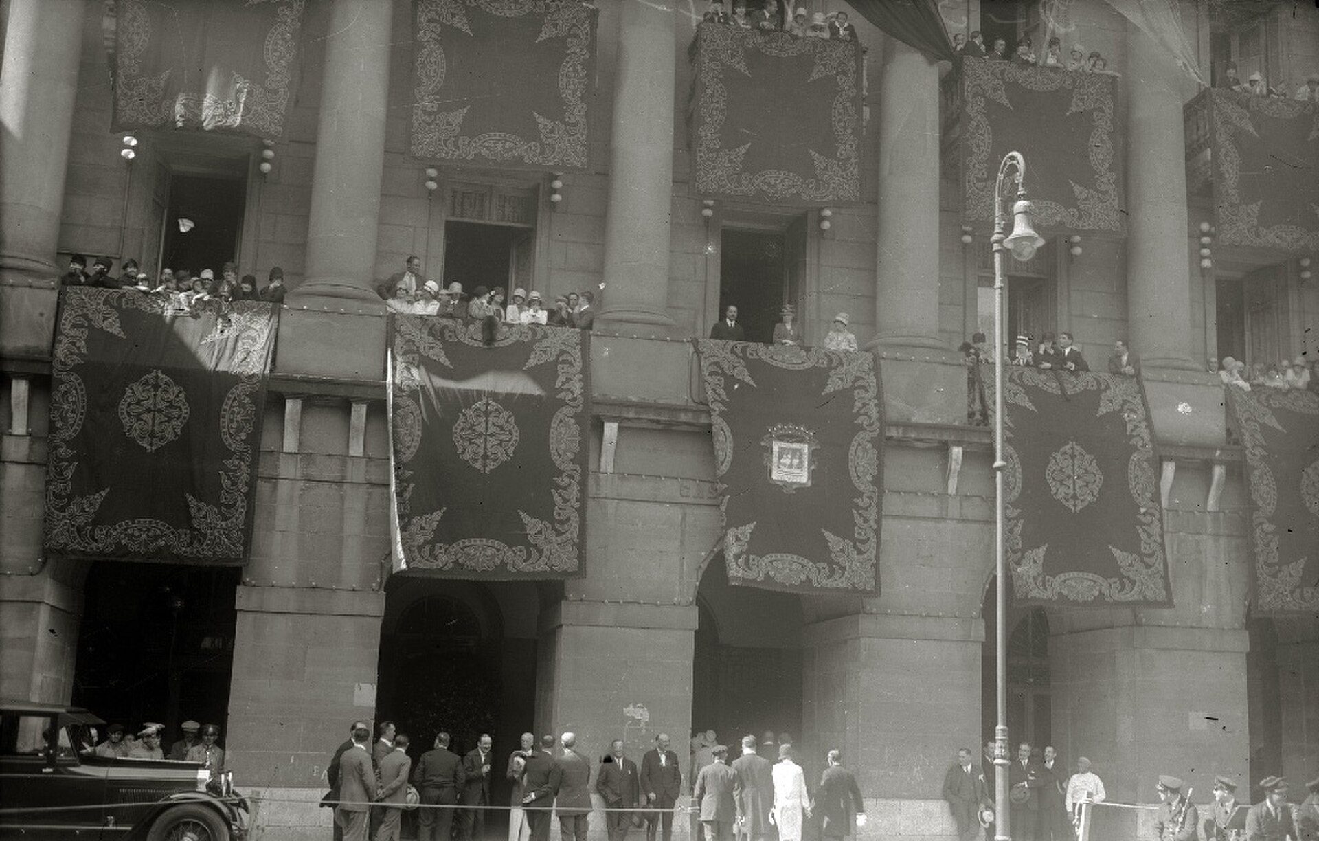 Historic building with balconies, ornate banners, and a crowd gathered outside.