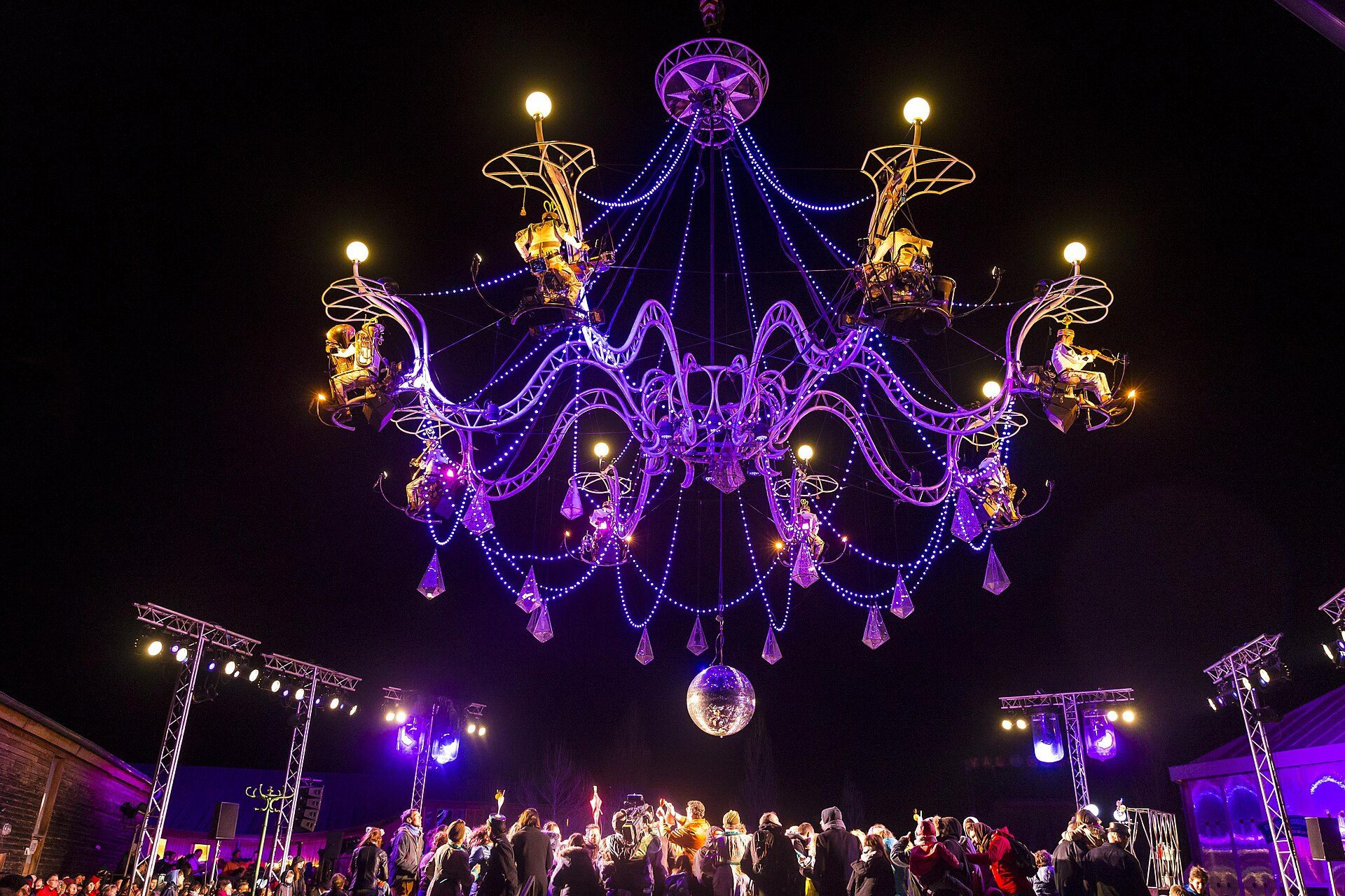 A large, ornate chandelier with purple lights and a disco ball in a festive room.