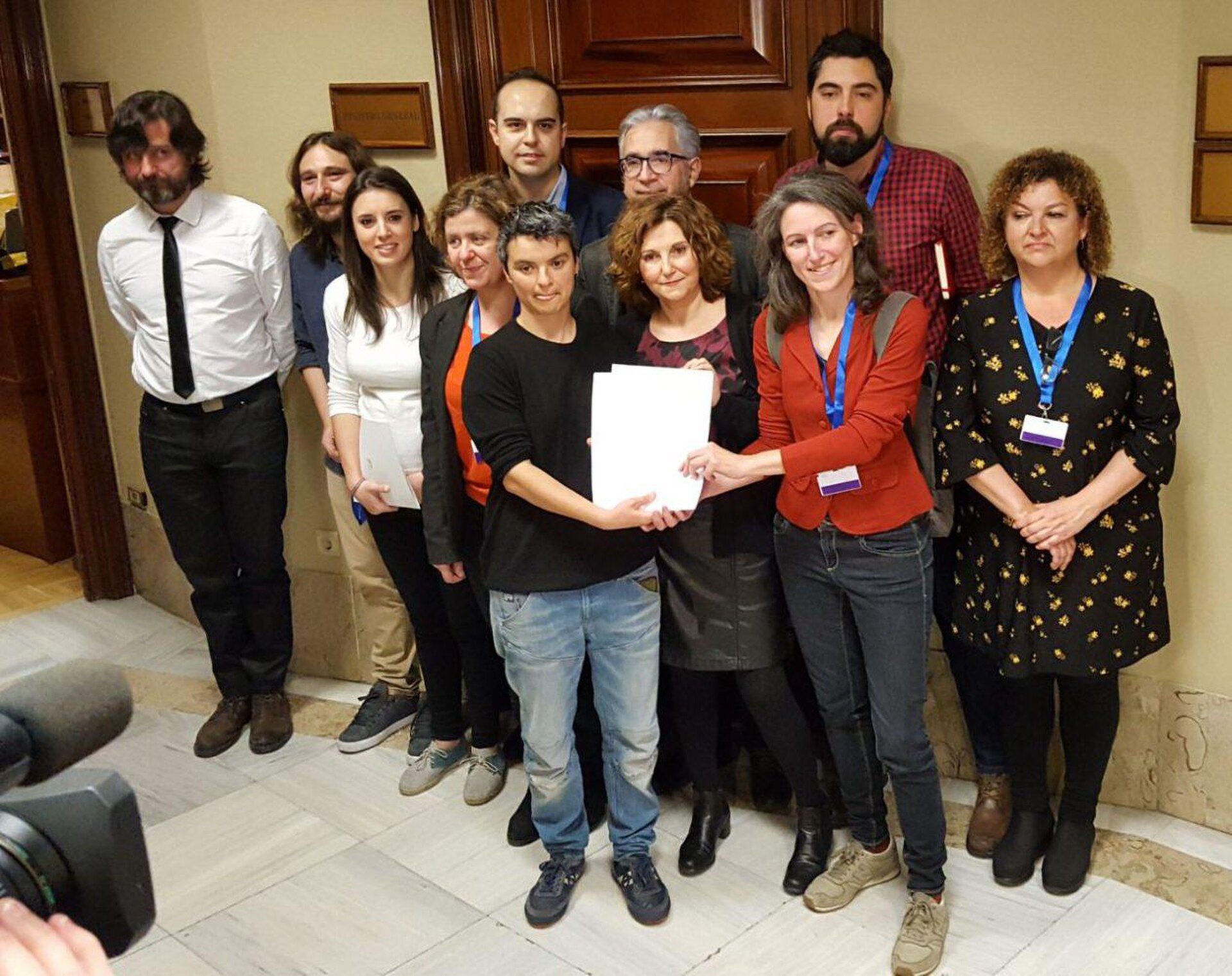 A group of people posing for a photo in a conference room with a wooden door and a camera.