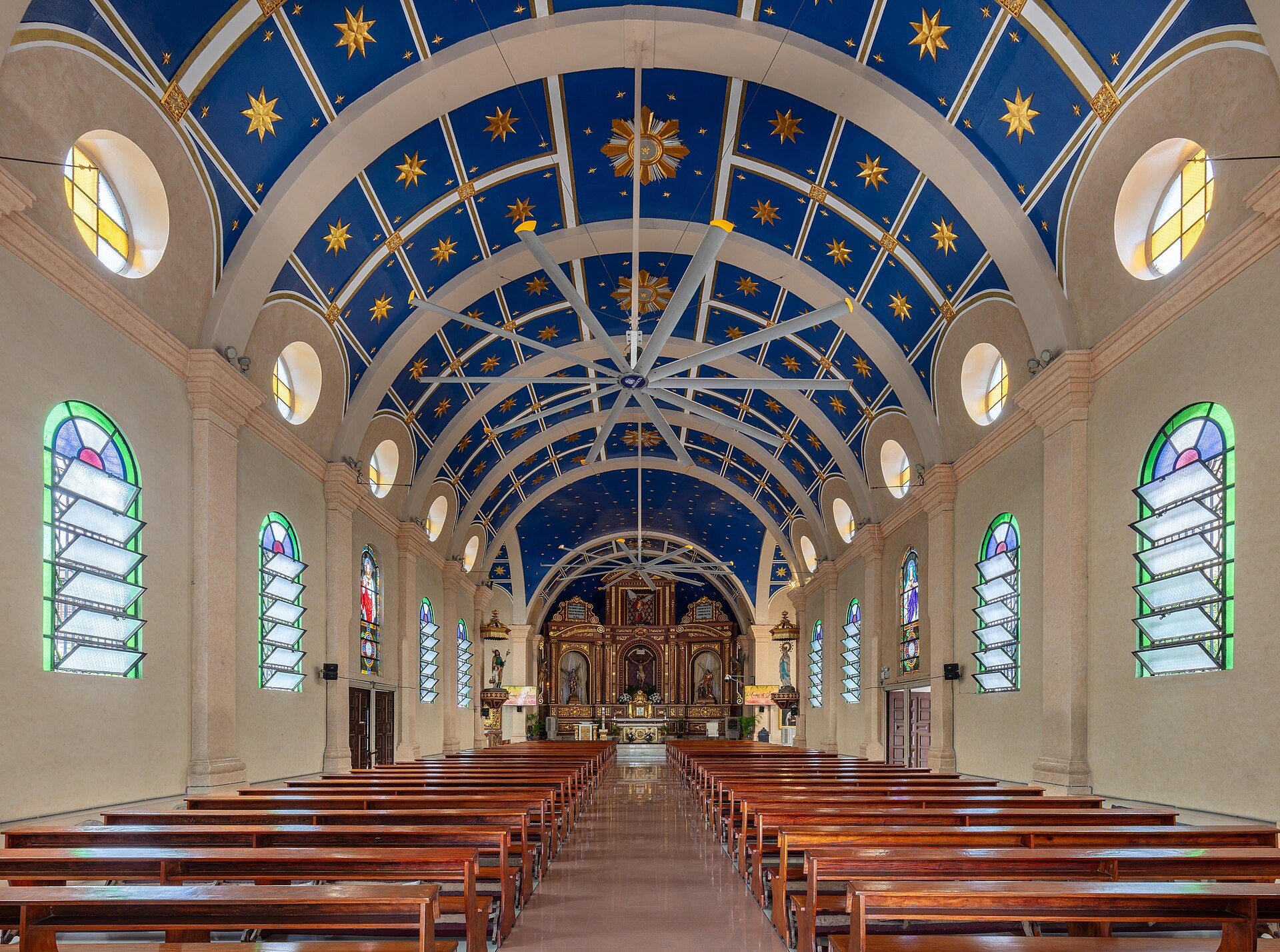 Interior view of a church with wooden pews, stained glass windows, and a blue starry ceiling.