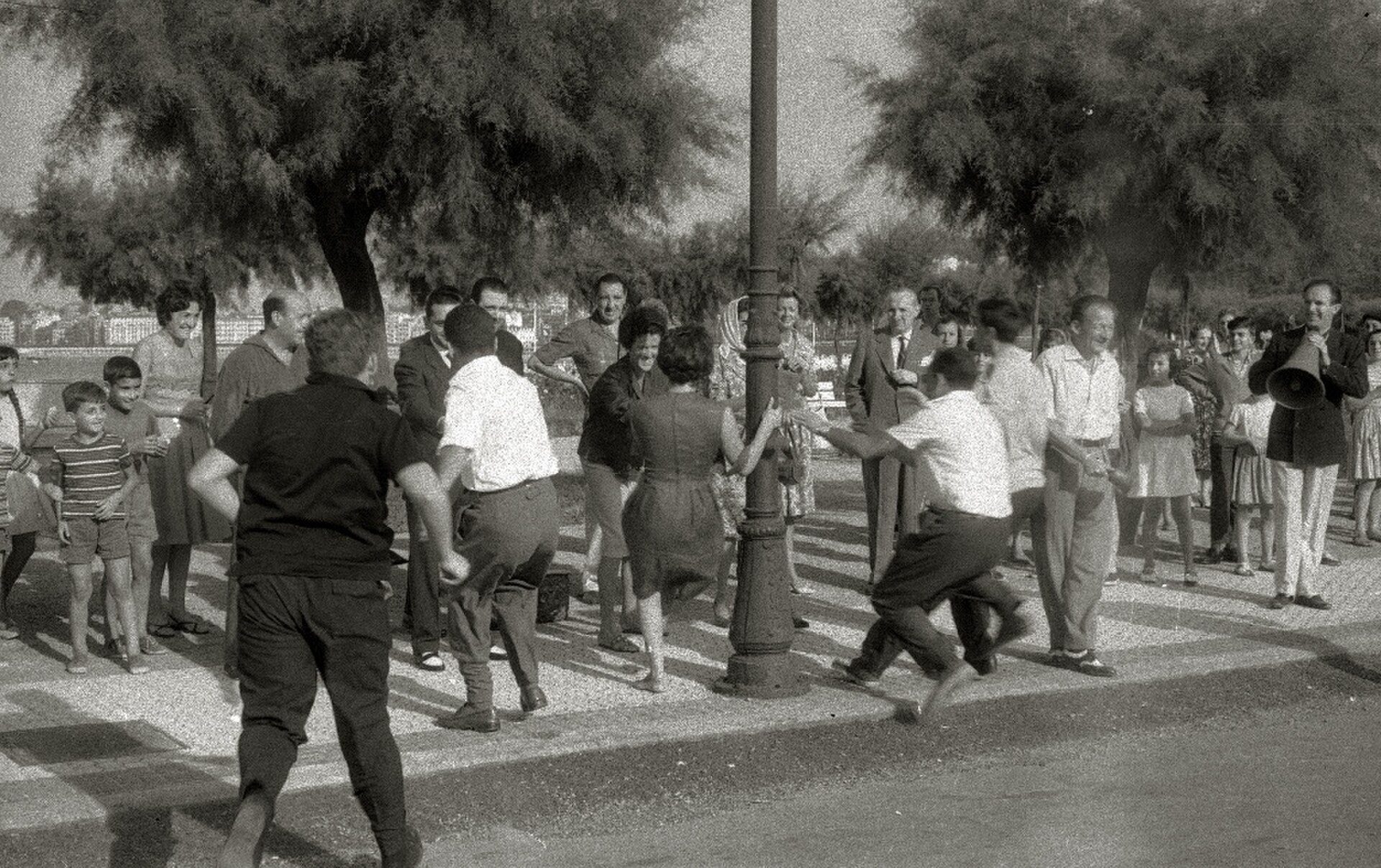 Alt text: Black and white photo of a lively street scene with people crossing the road.