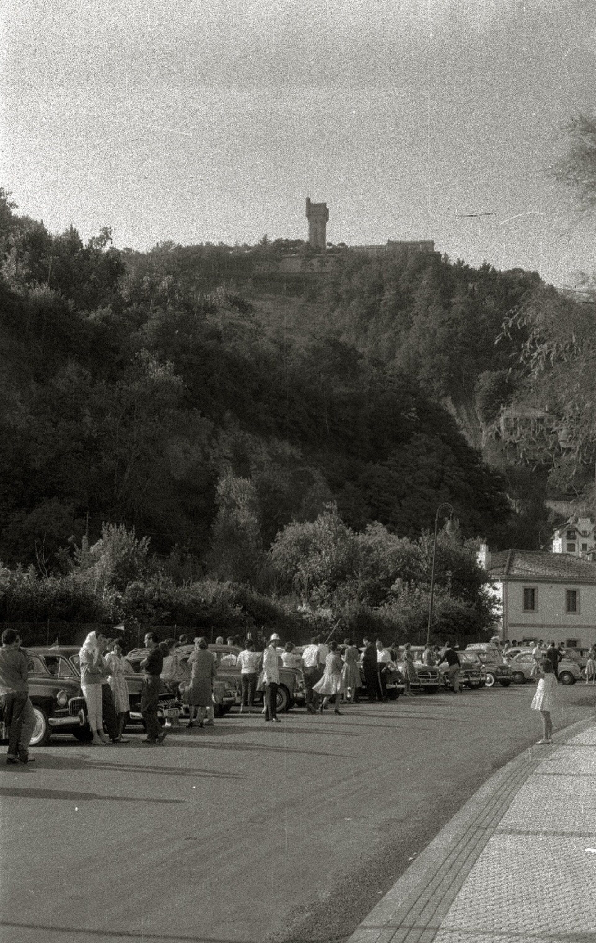 Alt text: "Parking lot with people, scenic hillside view, and a monument in the background.