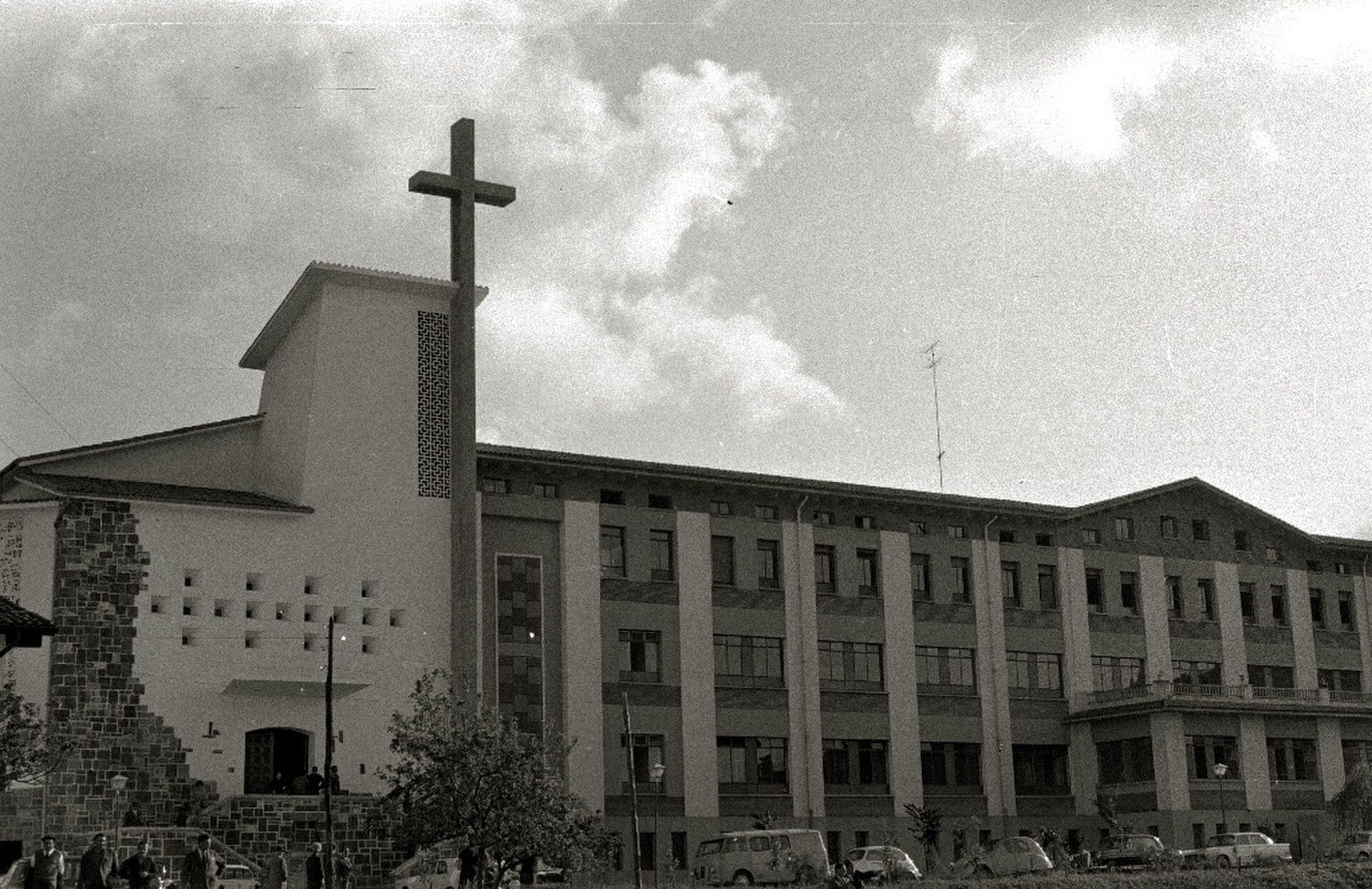 A large church with a cross, surrounded by a parking lot and trees.