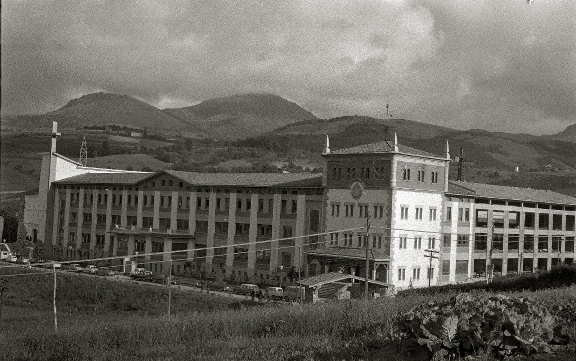 A large, multi-story building with a mountain view, featuring balconies and a central tower.
