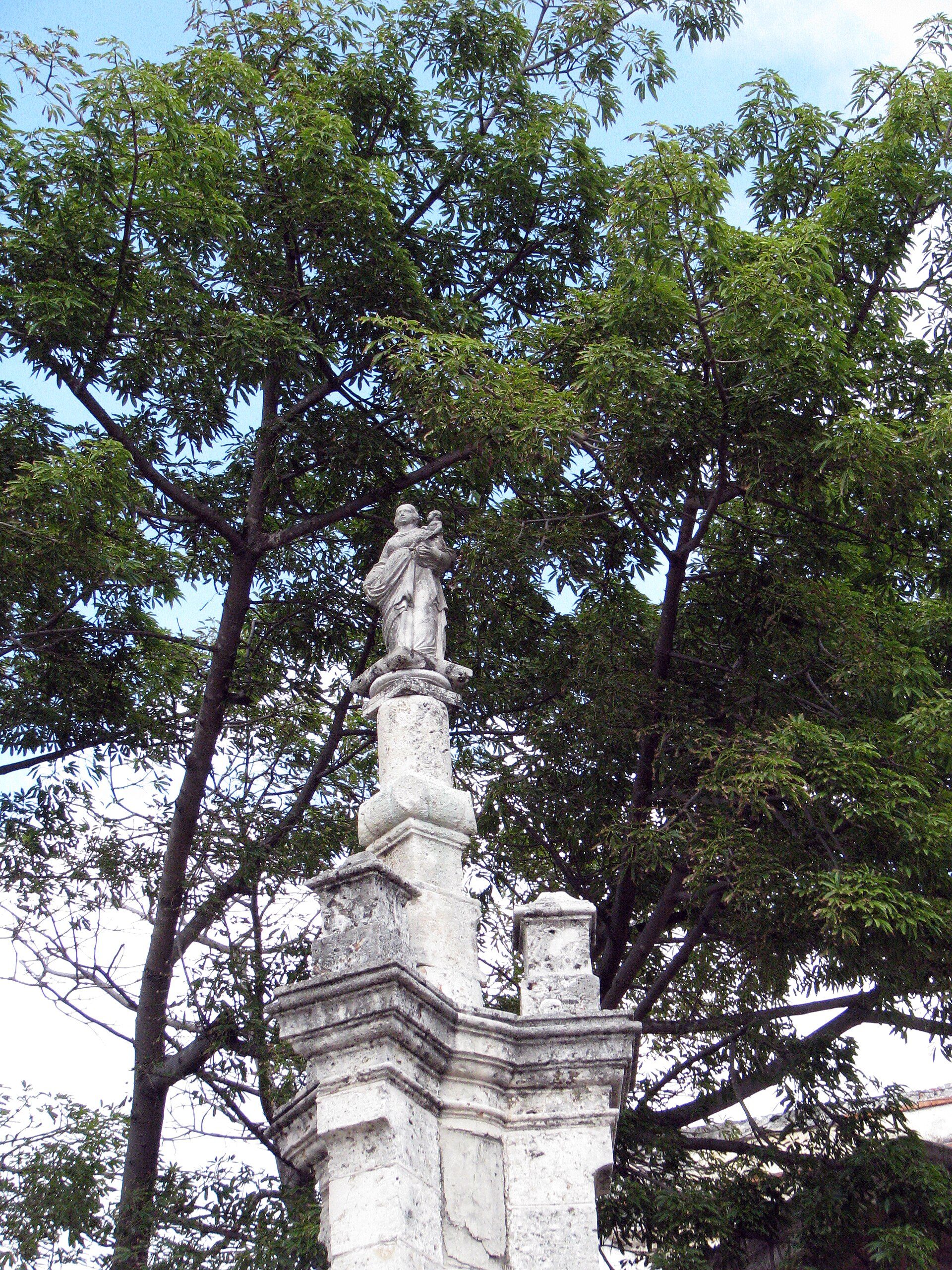 Alt text: Outdoor statue of a figure on a pedestal, surrounded by lush green trees.