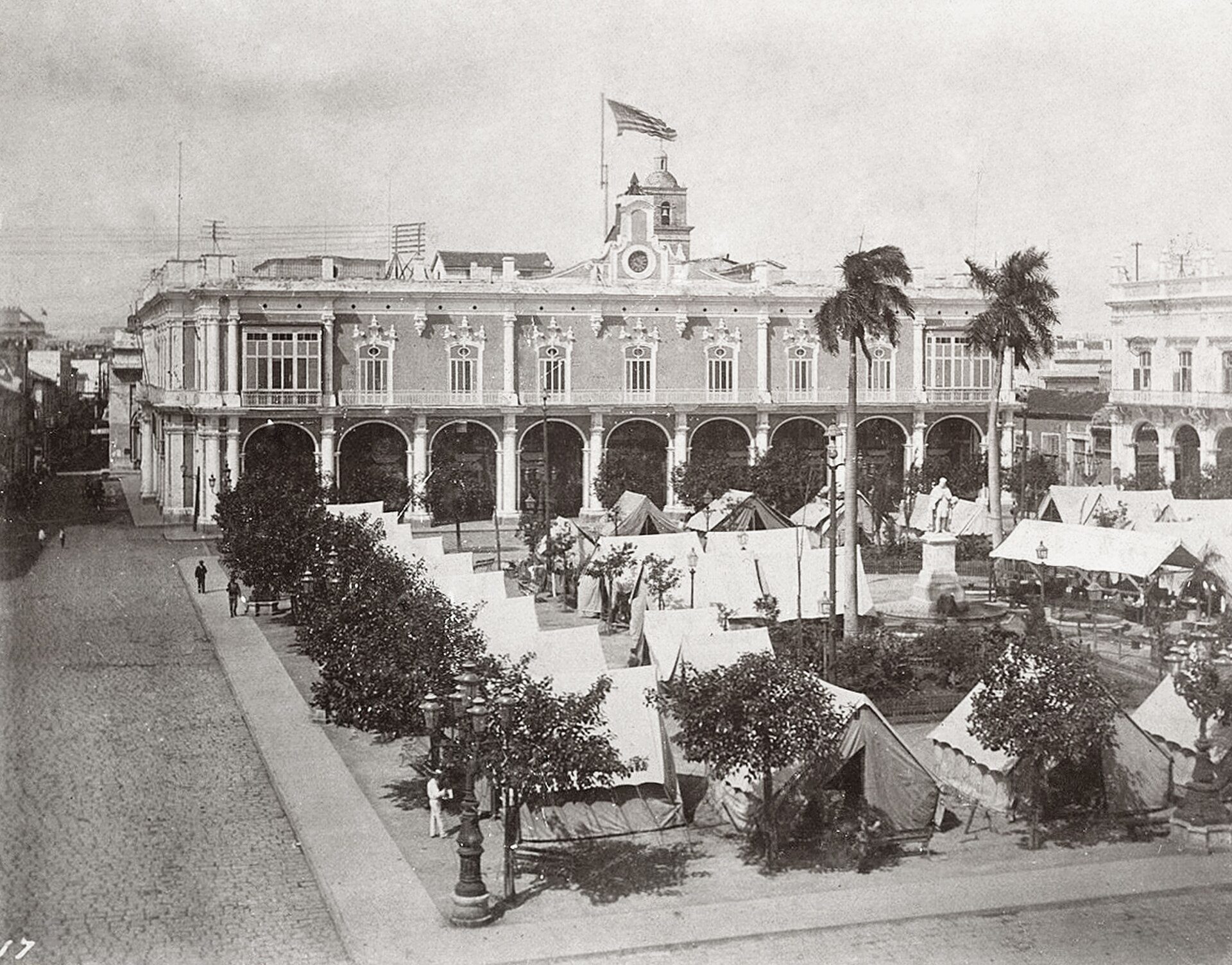 Historic building with arched windows, palm trees, and tents in front.