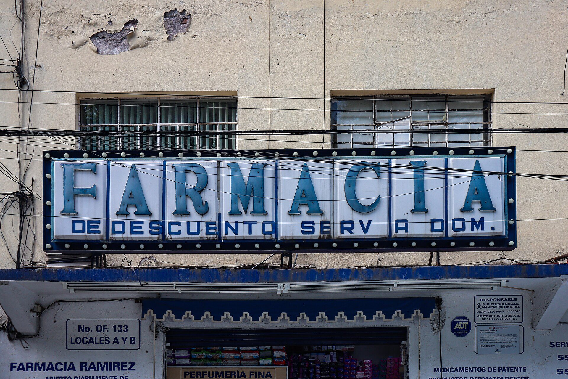 Alt text: A pharmacy sign with "FARMACIA DE DESCUENTO SERV A DOM." in blue letters on a white background.