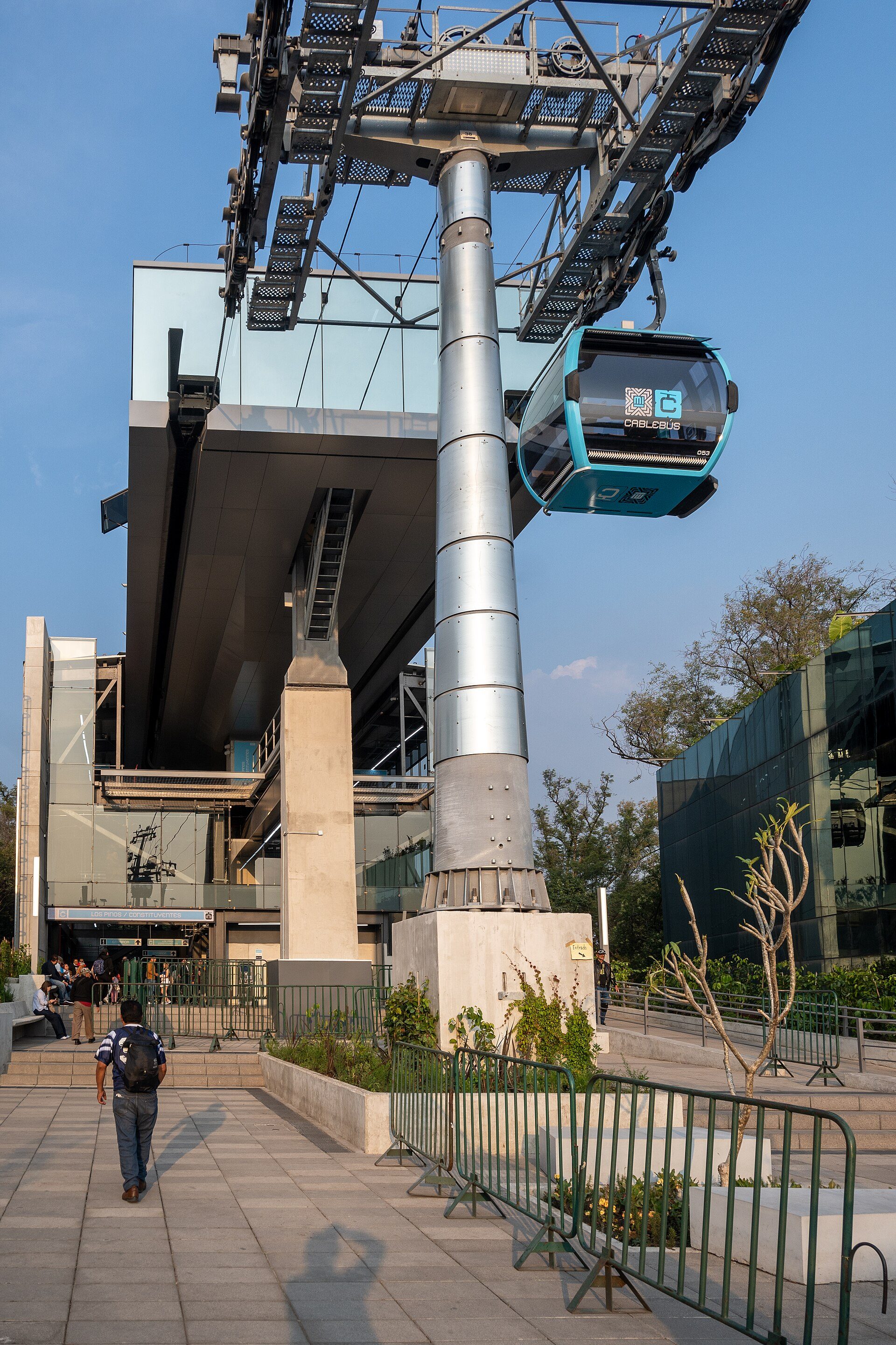 Modern cable car station with blue cab, glass building, and landscaped area.