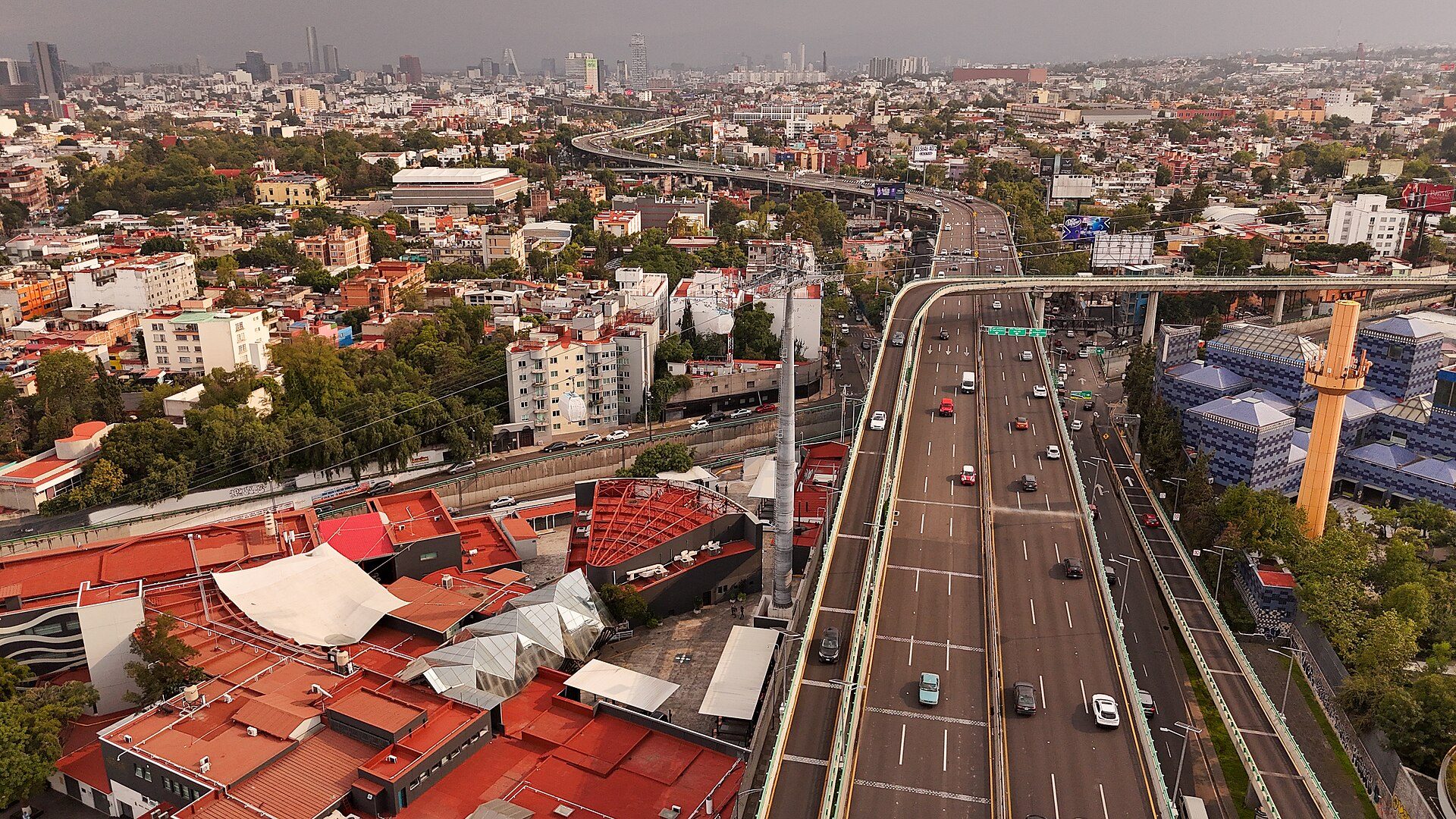 Aerial view of a cityscape with a highway, buildings, and greenery.