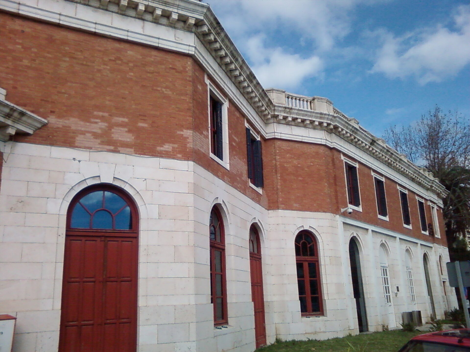 Alt text: Two-story brick building with arched windows and red doors, featuring a classic architectural style.