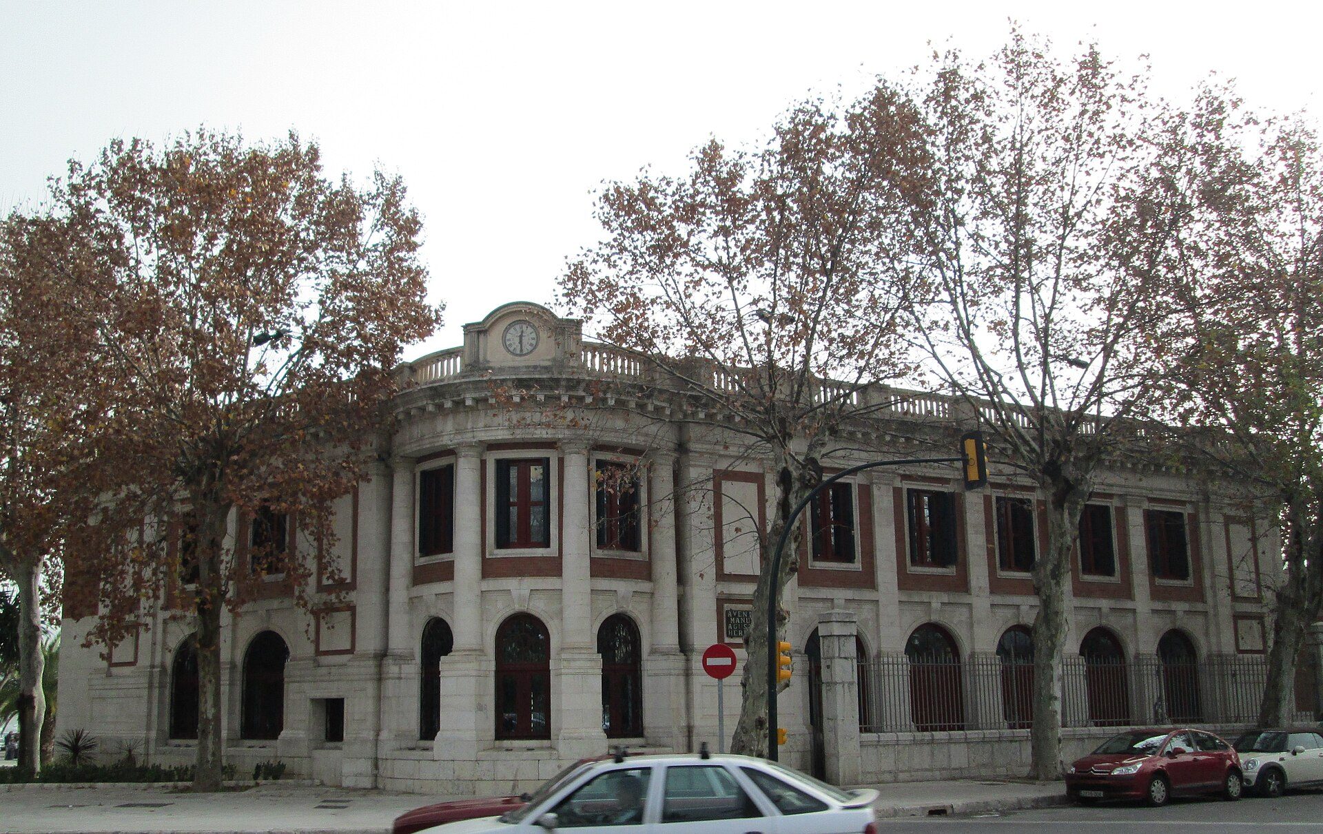 A historic building with arched windows, a clock, and leafy trees.