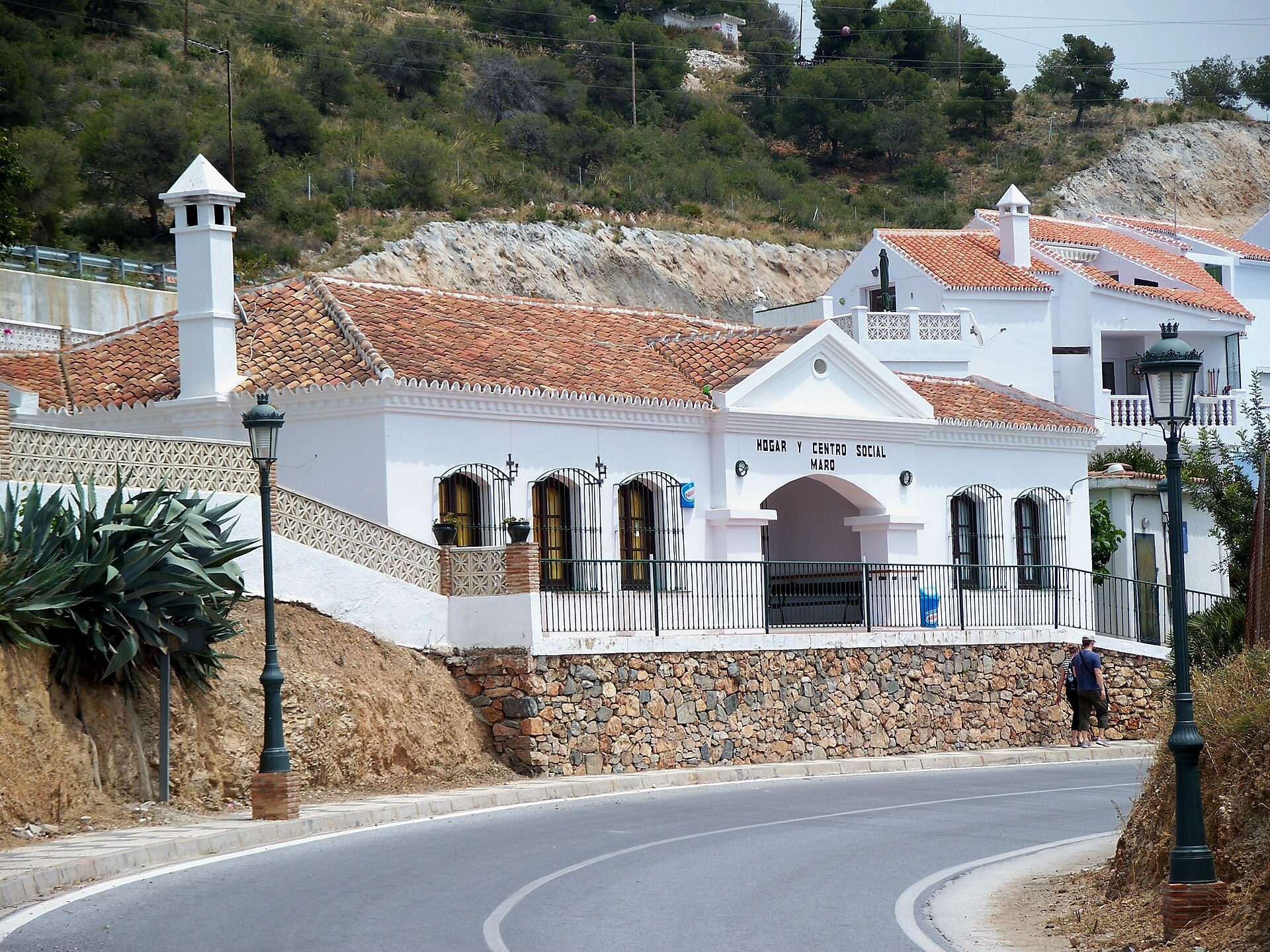 Traditional white house with red roof, stone walls, and scenic hillside view.