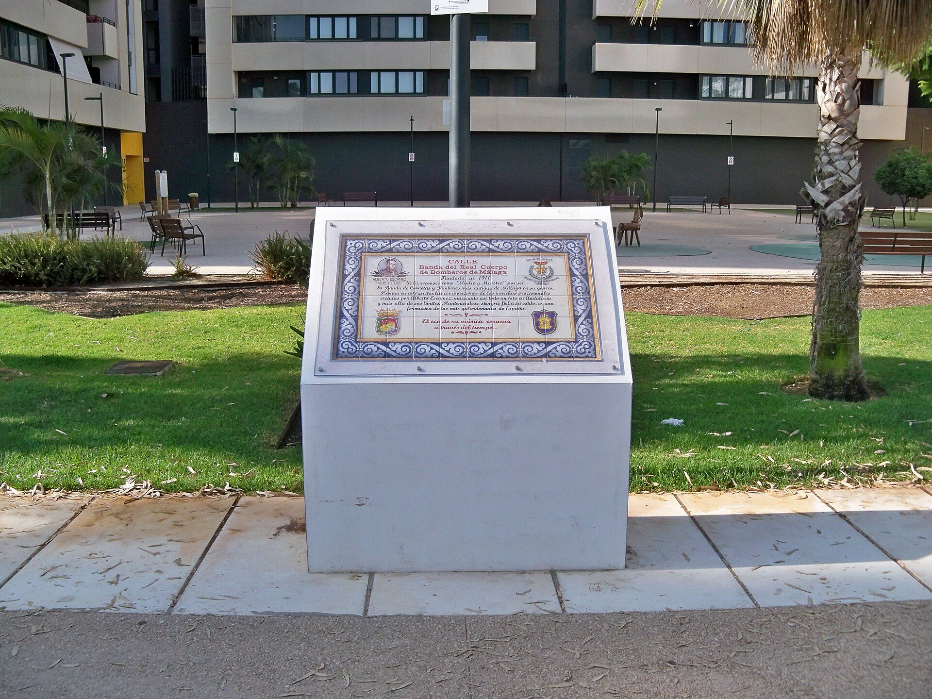 A white monument with a plaque in a park setting, surrounded by green grass and trees.