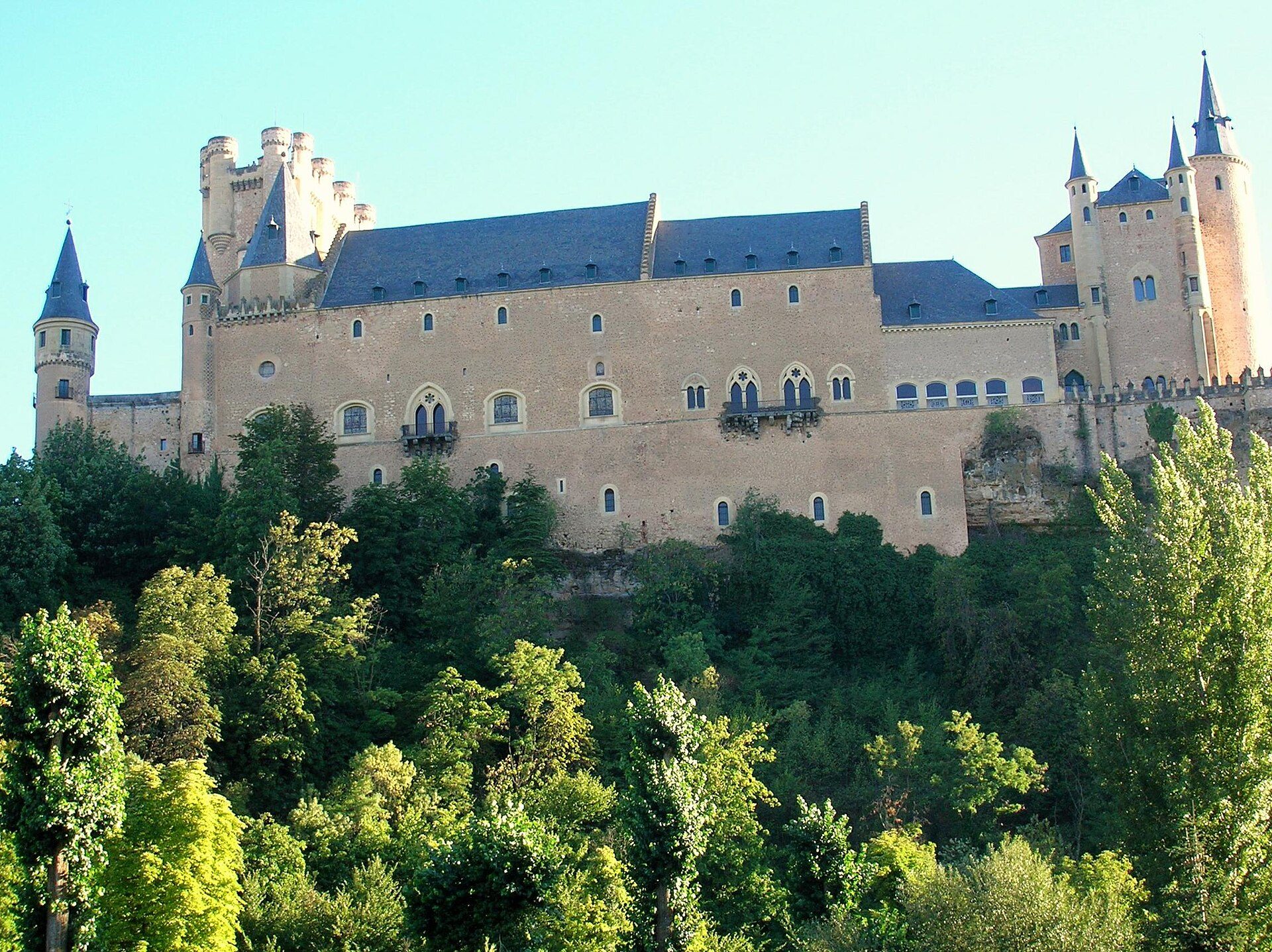 A medieval castle with multiple towers and a lush green forest view.