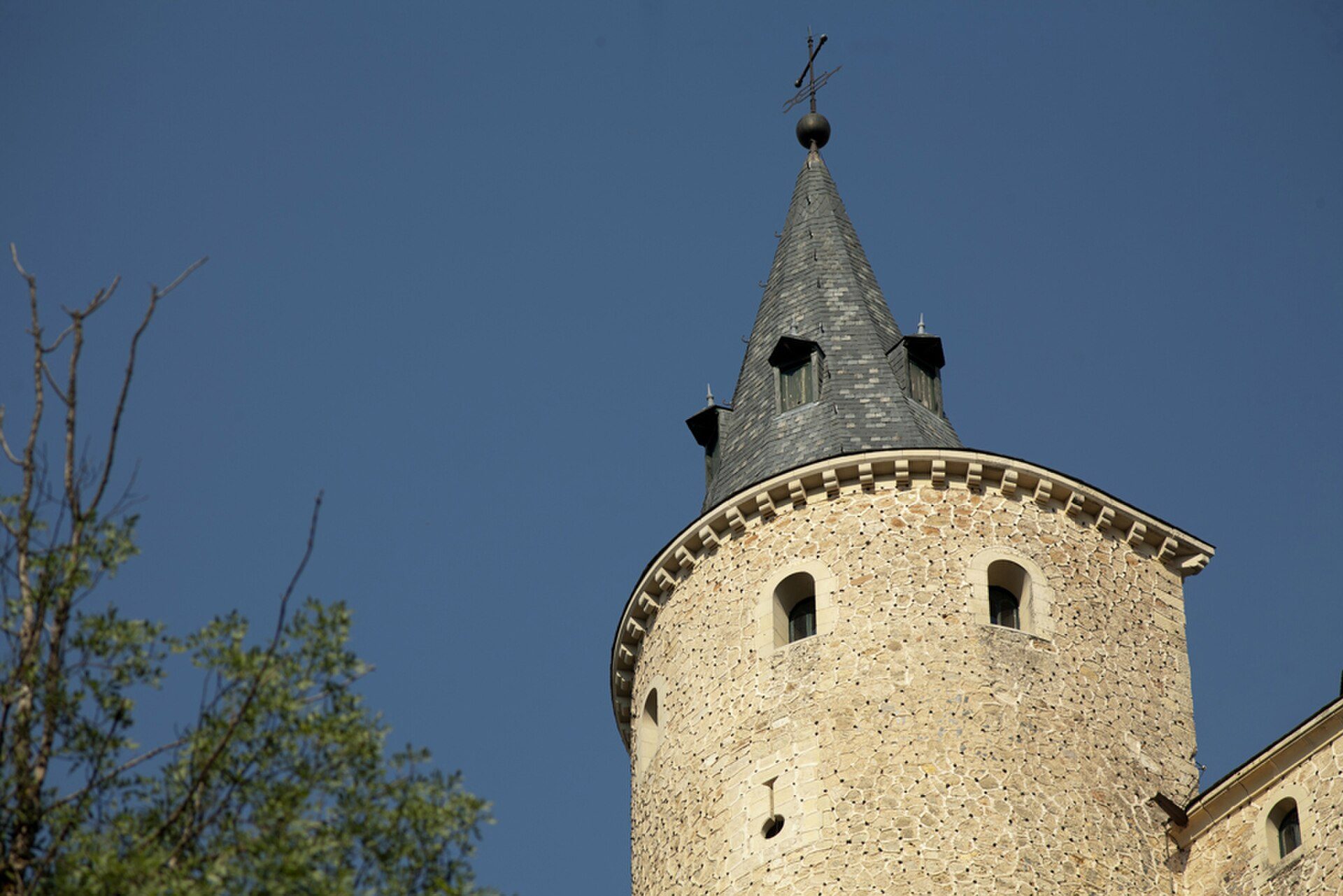 A stone tower with a conical roof and small windows, set against a clear blue sky.