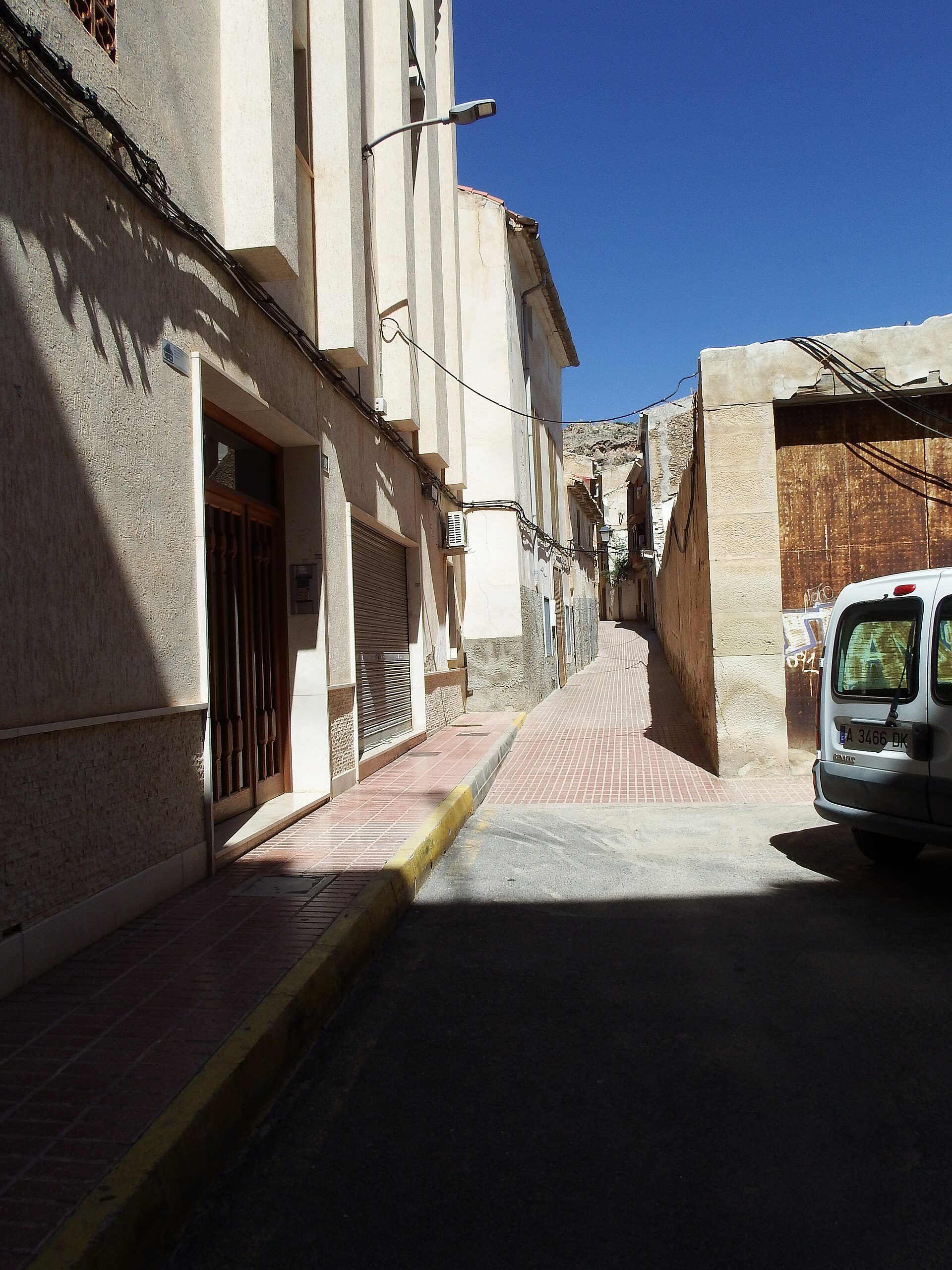 Narrow alley with beige buildings, clear blue sky, and a parked van.