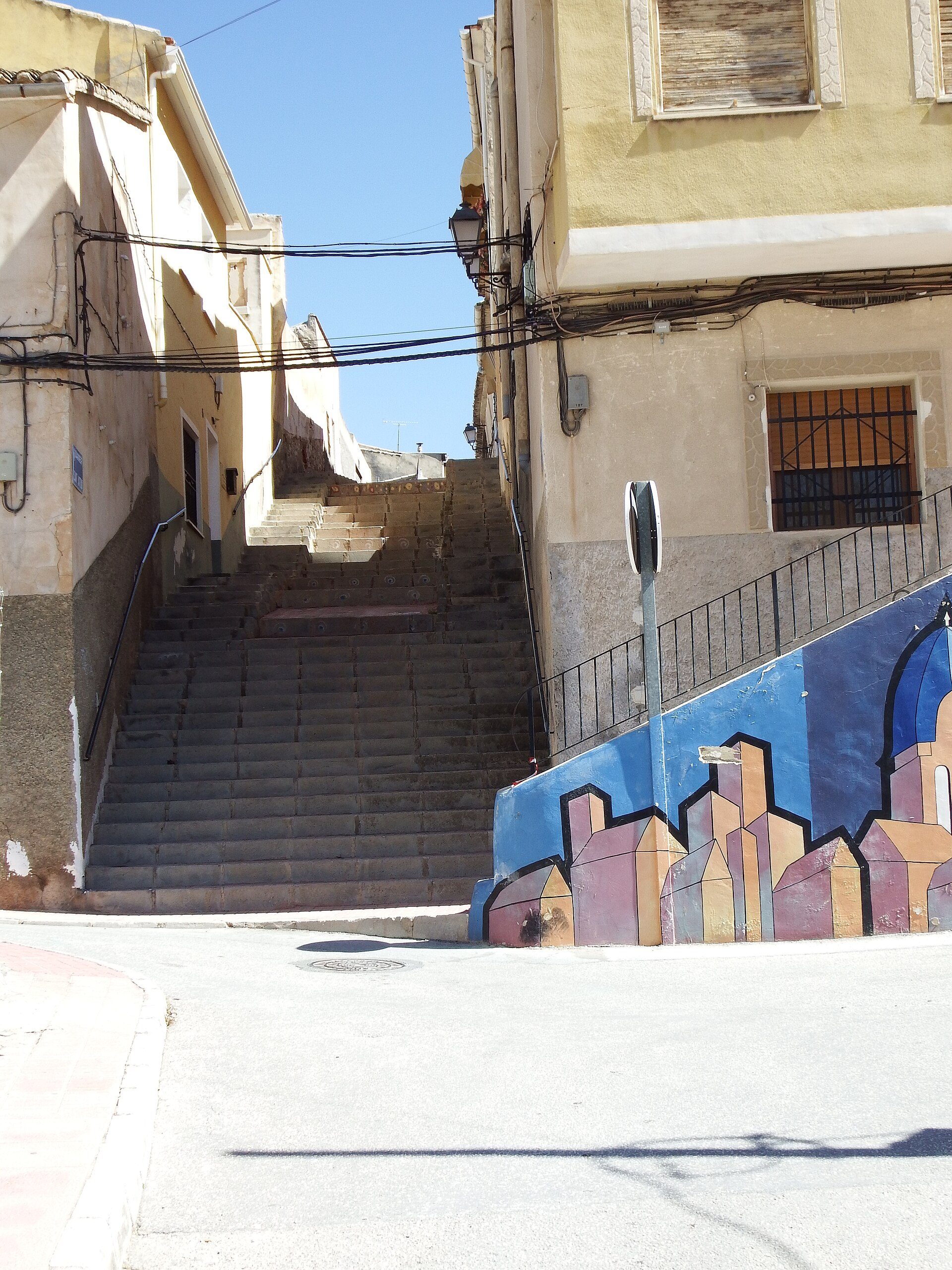 Alt text: Narrow street with stairs, colorful mural, and old buildings.
