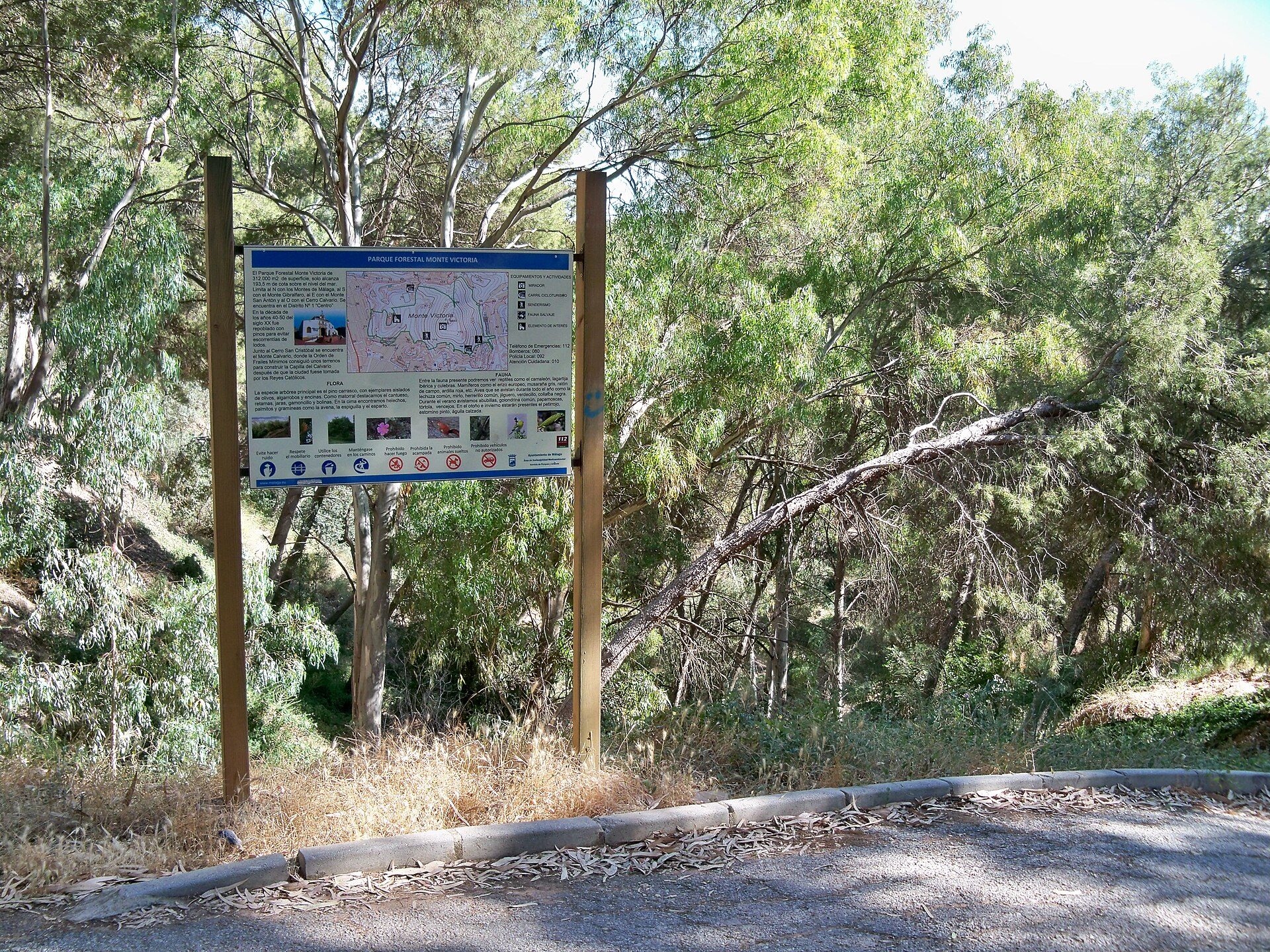 A park sign with a map and images of a nature trail surrounded by trees.