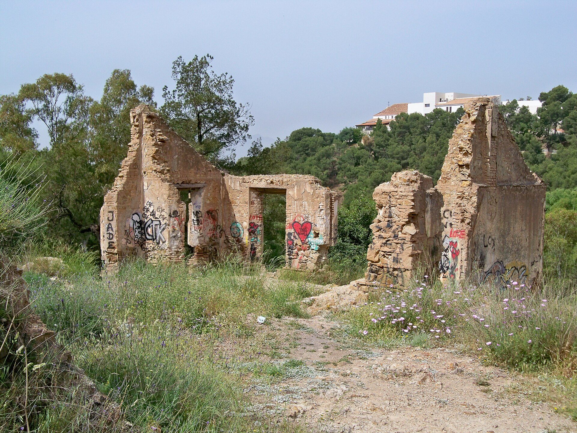 Abandoned, graffiti-covered ruins with overgrown vegetation and distant buildings.